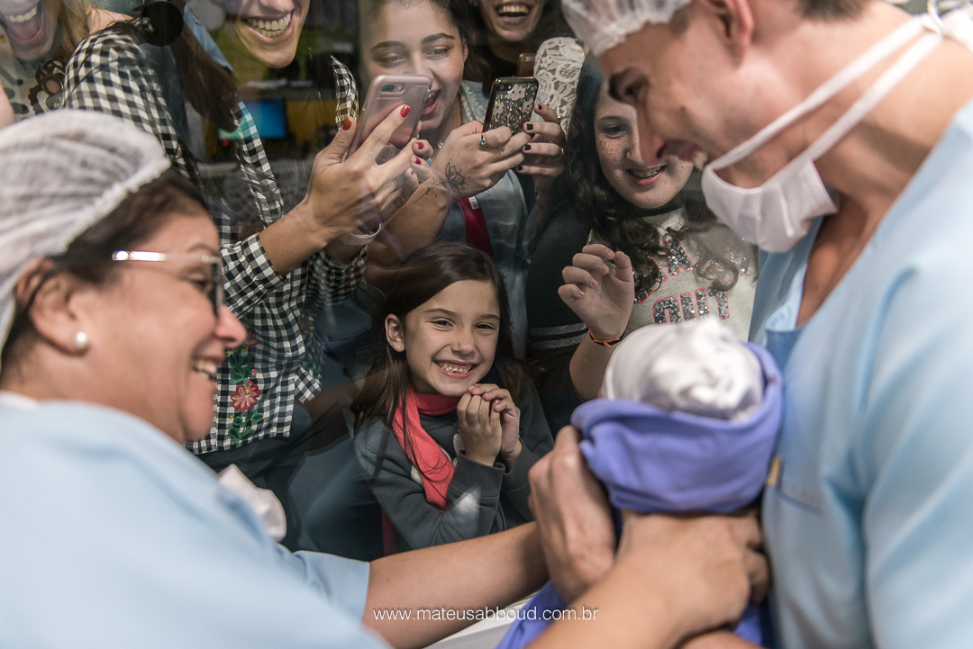Pai e pediatra mostrando o bebê pela primeira vez através do vidro no bercário. Família tirando muitas fotos.