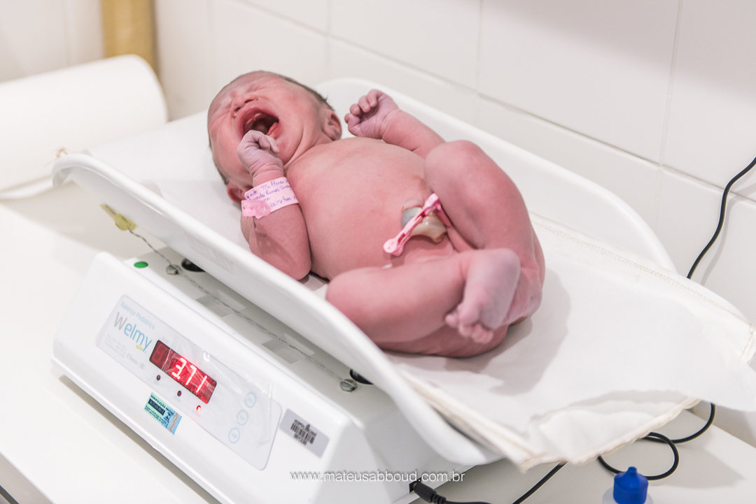 Bebê sendo pesado na balança após o parto.