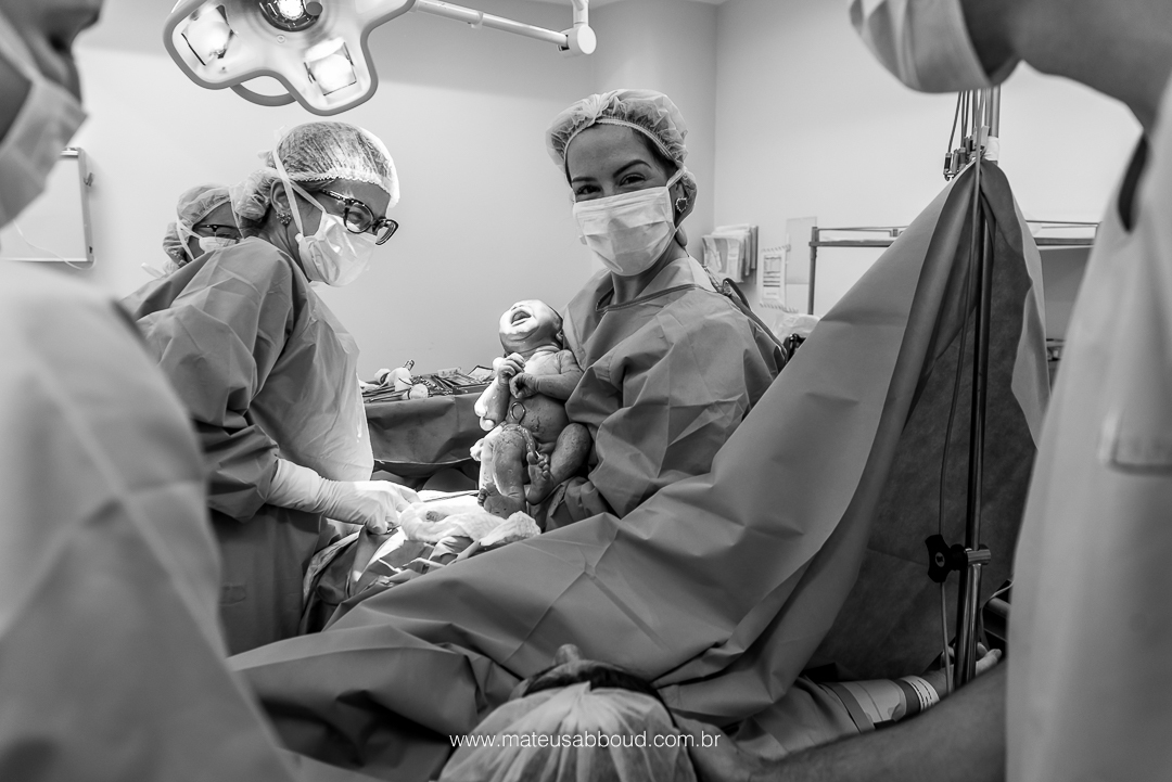 Obstetra com o bebê no colo mostrando para os pais pela primeira vez.