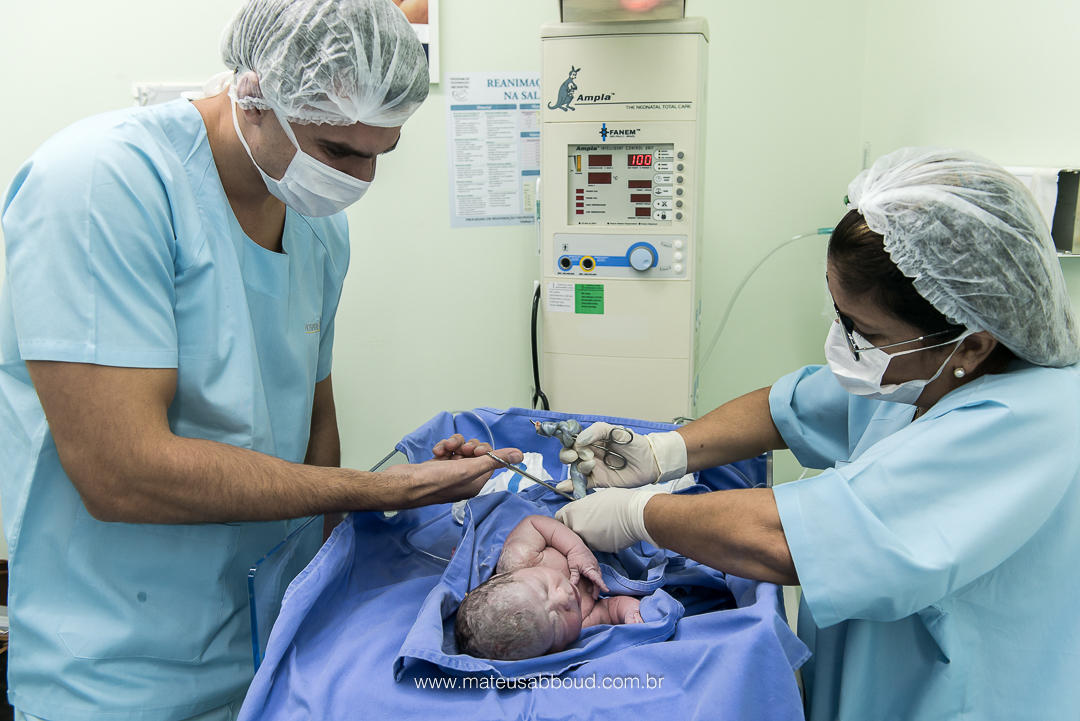 Pai e pediatra cortando o cordão umbilical do bebê após o parto.