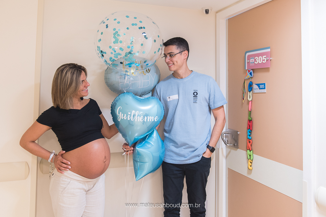 gestante e marido na porta do quarto da maternidade segurando balões com o nome do bebê guilherme