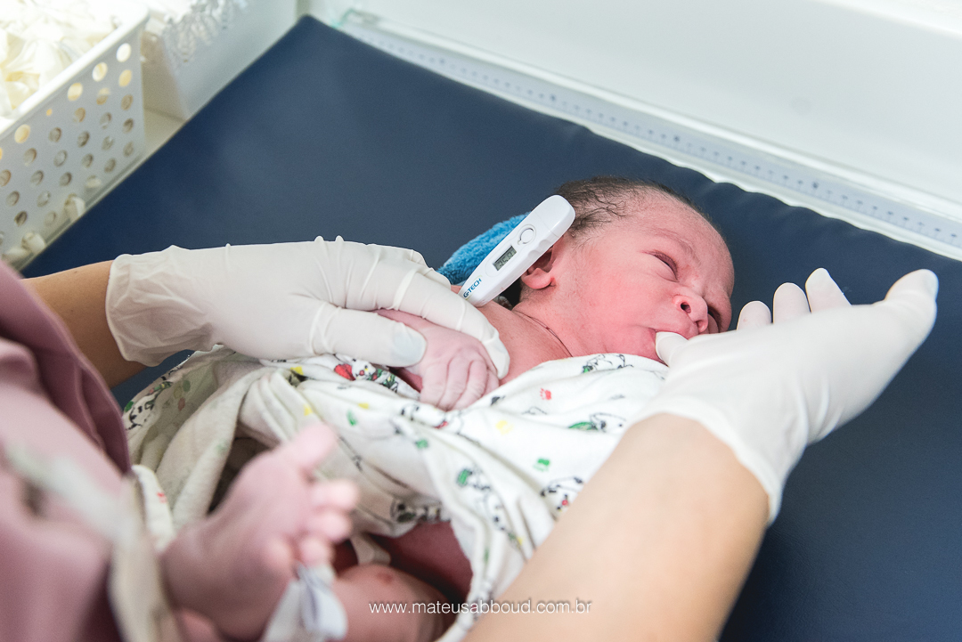 enfermeira medindo a temperatura do bebê guilherme enquanto ele chupa o dedo da enfermeira que está de luva