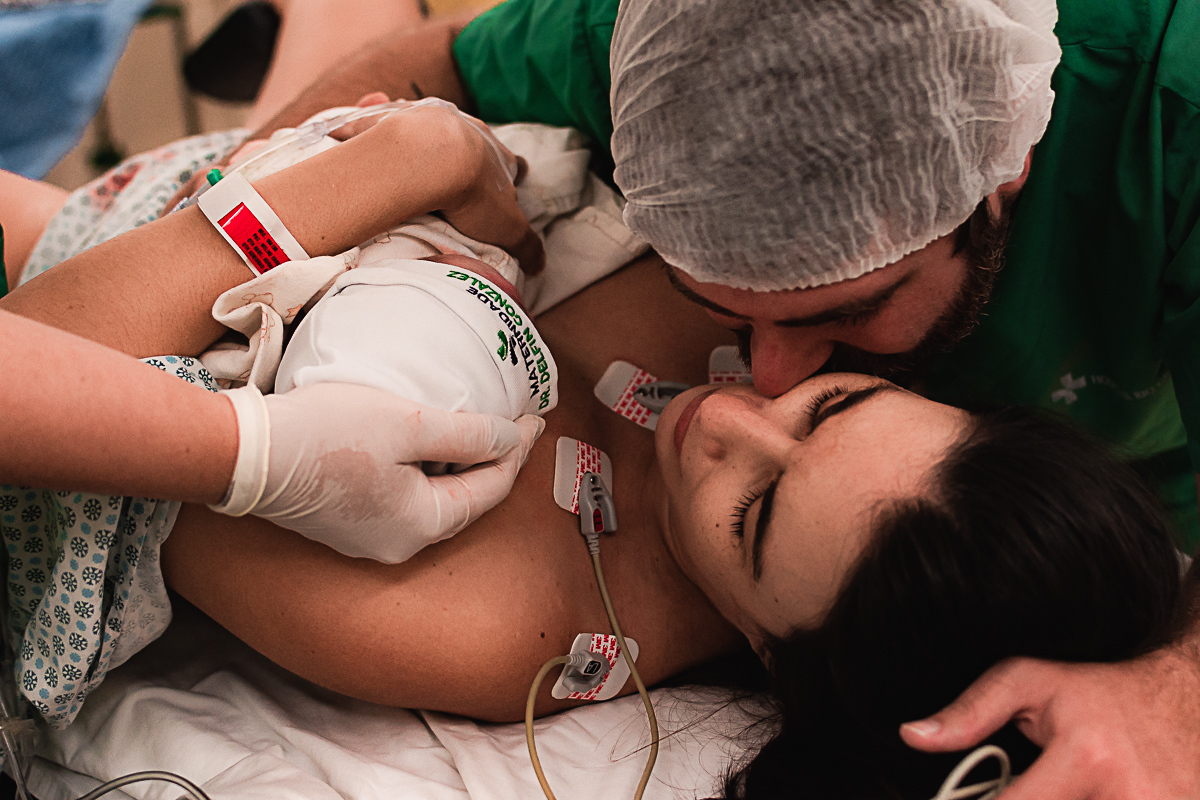 foto do pai dando carinho à mãe com o bebê no colo