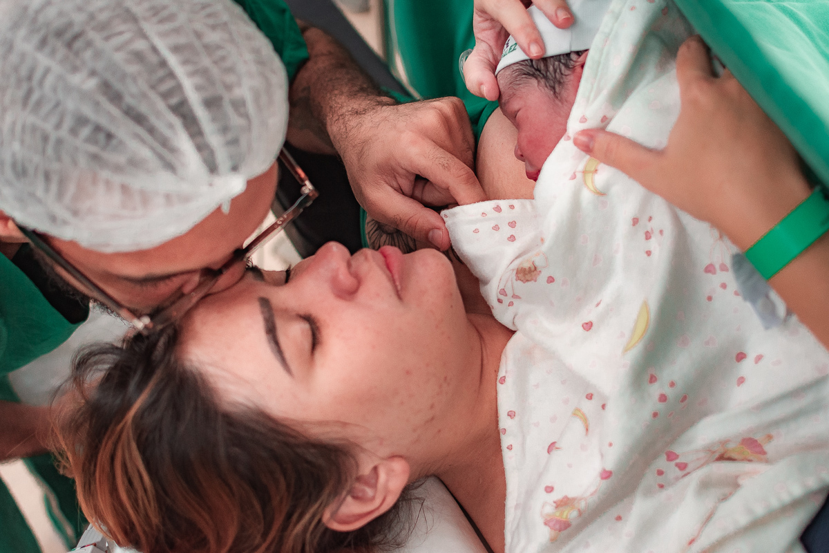 PAI DÁ CARINHO À MÃE ENQUANTO ELA SEGURA O BEBÊ QUE ACABOU DE NASCER