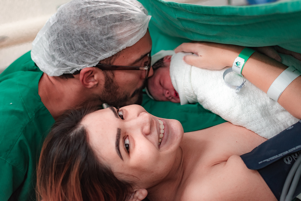 MÃE SORRIDENTE ENQUANTO PAI BEIJA O FILHO QUE ACABOU DE NASCER