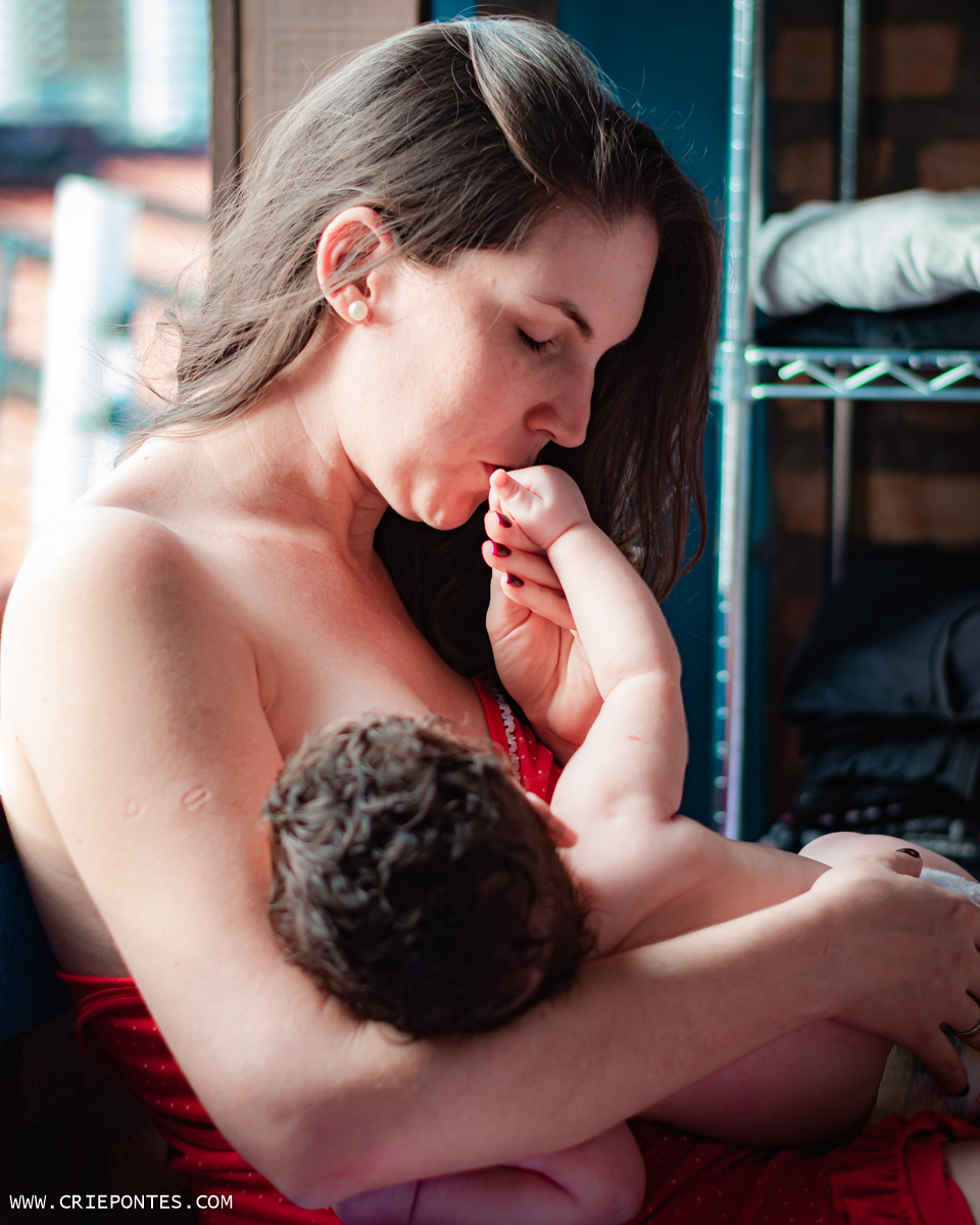 Mamãe beijando a mão do bebê enquanto ele mama