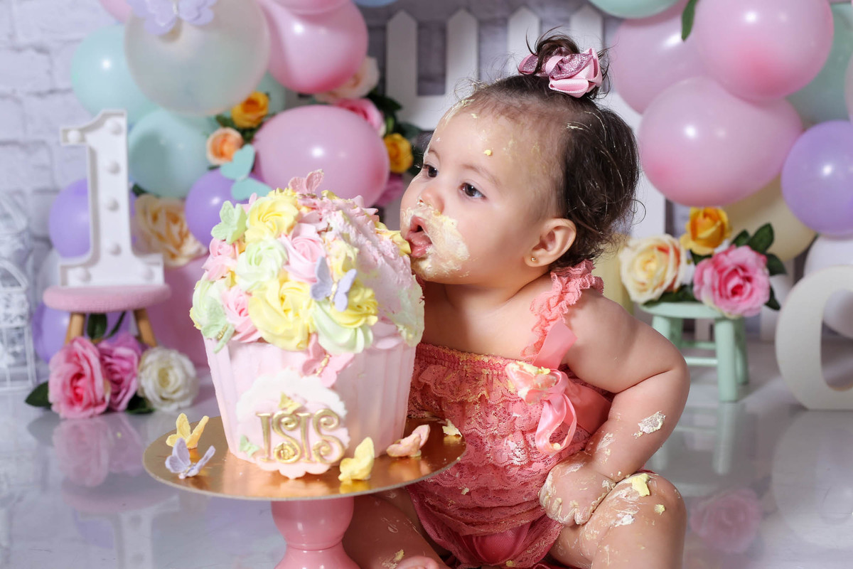 Foto sessão fotografica infantil menina comendo bolo personalizado com tema jardim e se lambuzando