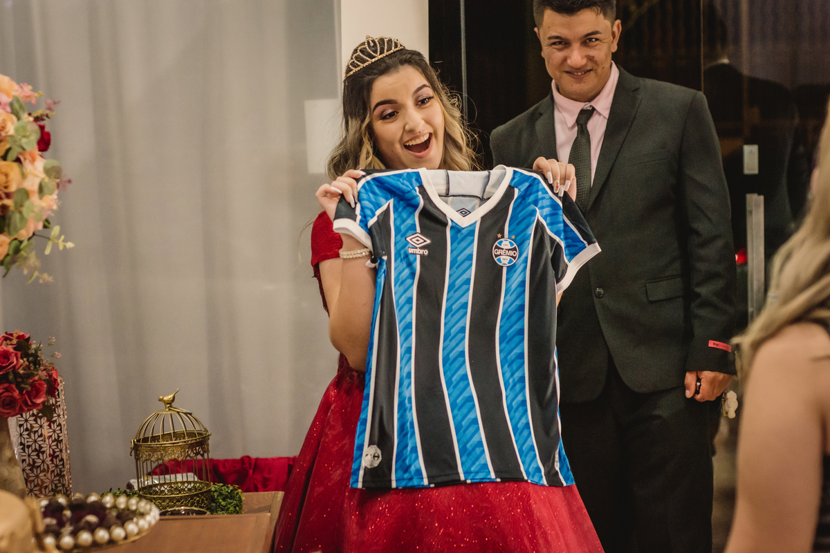 festa-de-debutante-festa-de-15-anos-fotografo-de-debutante-de-15-anos-em-são-leopoldo-no-vale-dos-sinos-vestido-vermelho-aniversário-mostrando-presente-camisa-do-grêmio-para-amiga