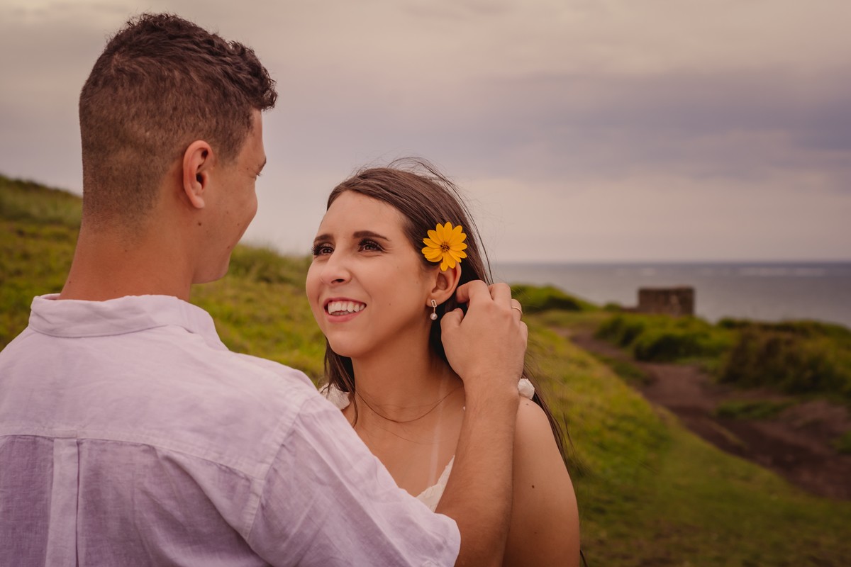 fotografo profissional de casamento em sao leopoldo fotografia autoral e diferente na praia de torres fotos de casal pre wedding vestido noivos noivinha mar torres praia areia morro escada ondas colocando margarida no cabelo da noiva 