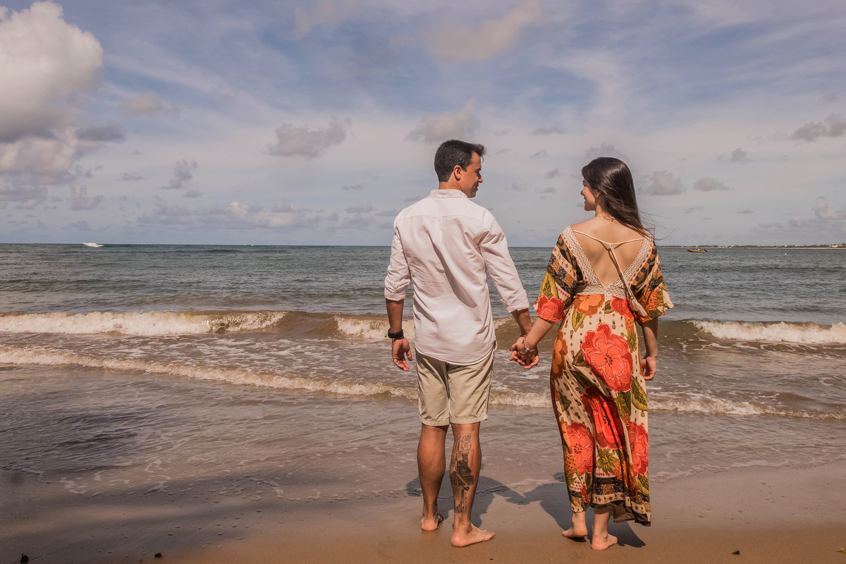 Casal caminhando de mãos dadas pela praia de Praia do Forte durante ensaio fotográfico na Bahia.