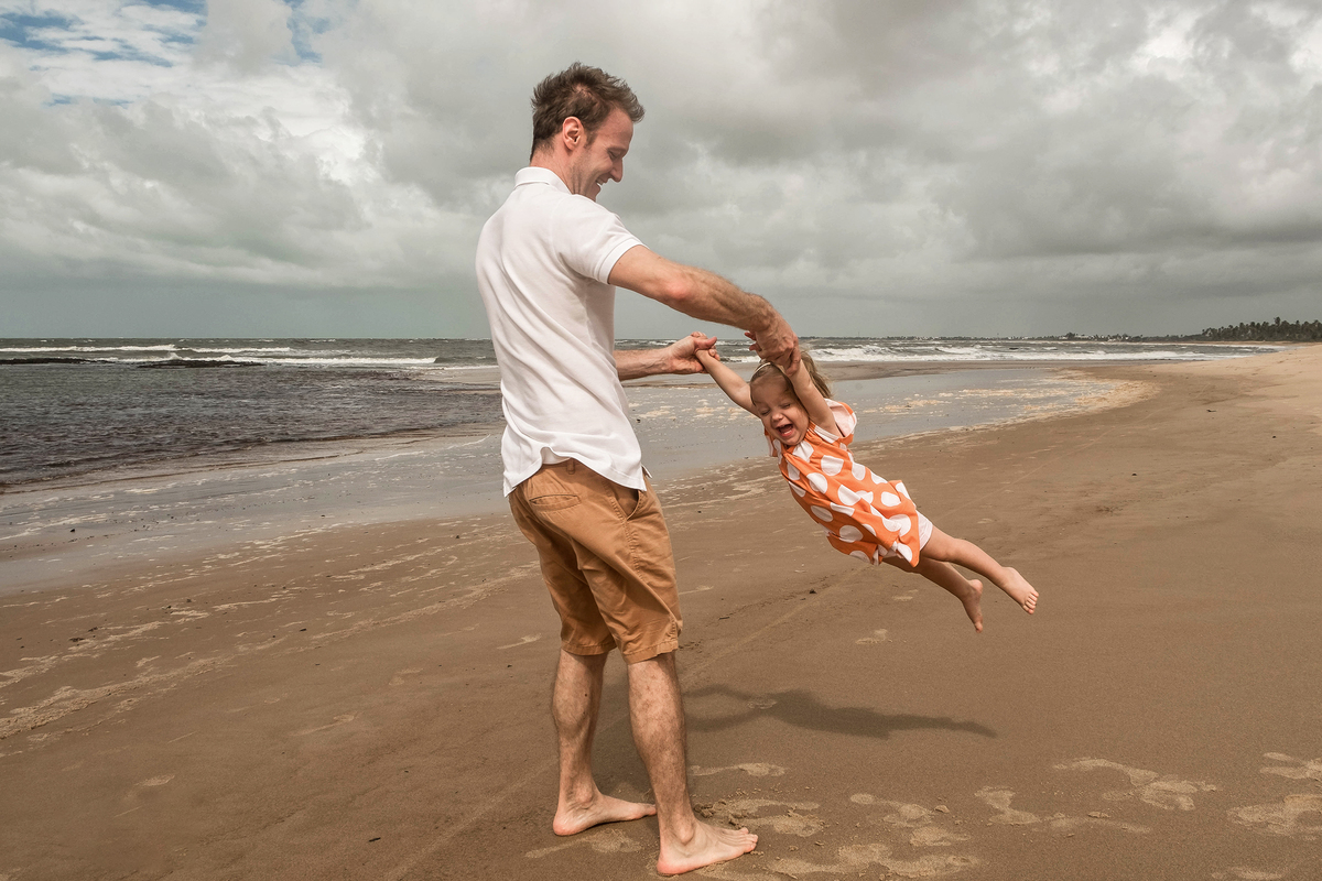 Denis com a filha pequena durante o ensaio fotográfico de família na praia em Praia do Forte, Bahia.