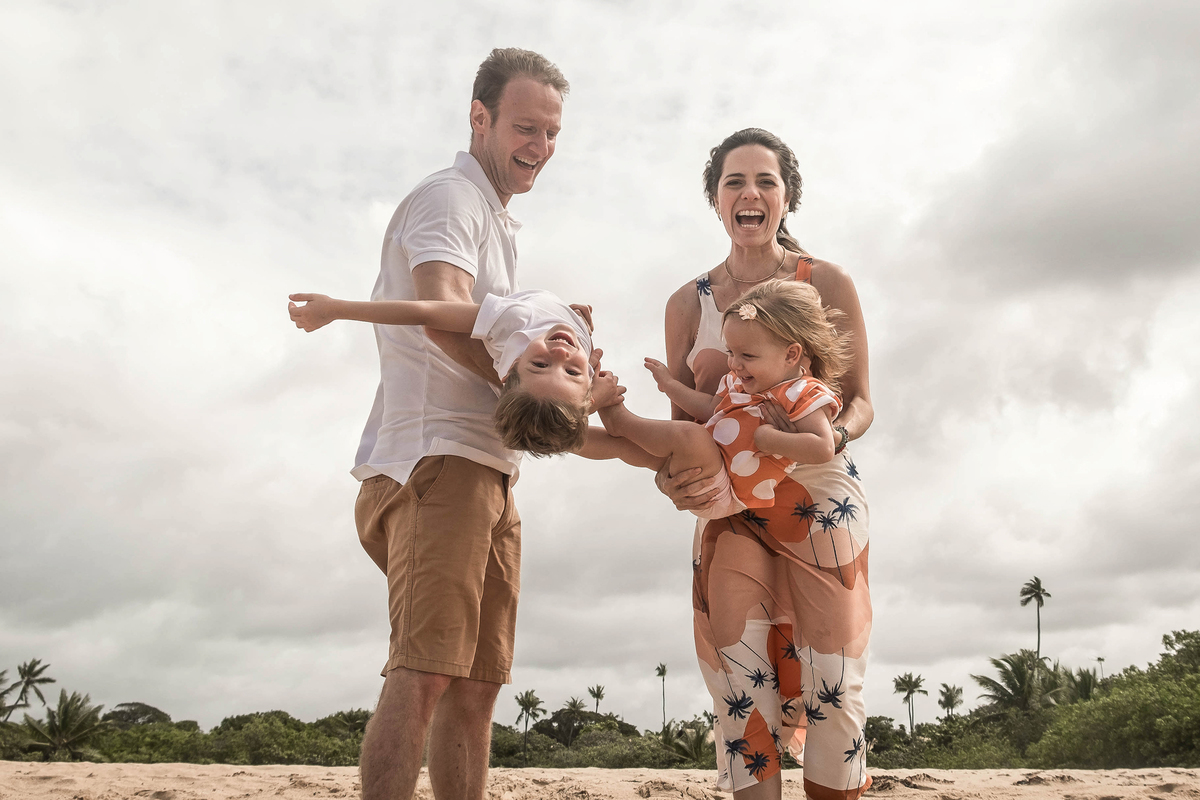 Mayara e Denis segurando os filhos em uma brincadeira de aviãozinho durante o ensaio de família em Praia do Forte.