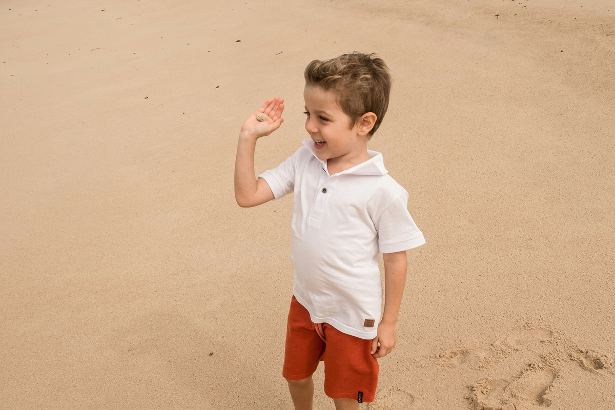 Menino de 4 anos mostrando uma concha encontrada na areia durante o ensaio de família em Praia do Forte, Bahia.