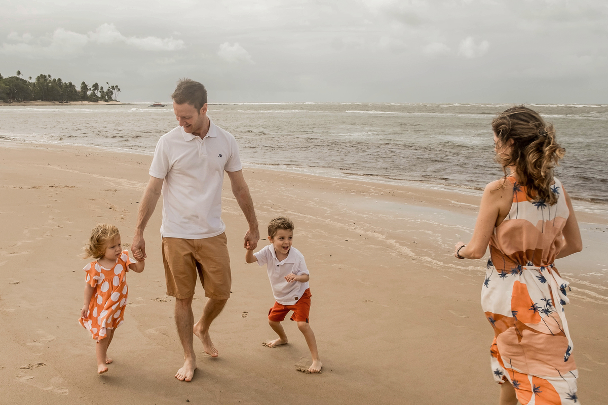 Mayara, Denis e os filhos caminhando juntos pela praia durante as férias em Praia do Forte.