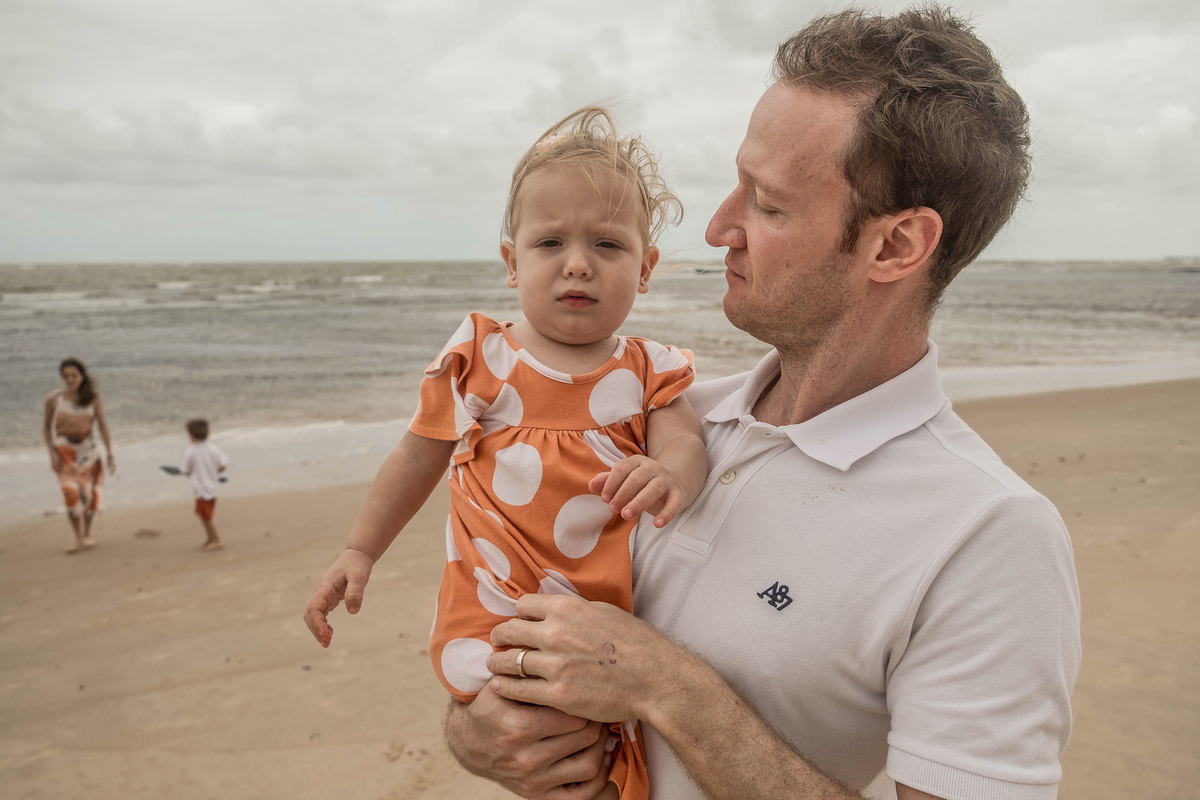 Denis com a filha pequena durante o ensaio fotográfico de família na praia em Praia do Forte, Bahia.