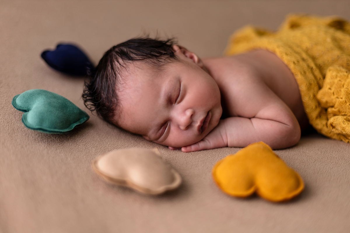 newborn deitado dormindo de bruços com corações de pelúcia