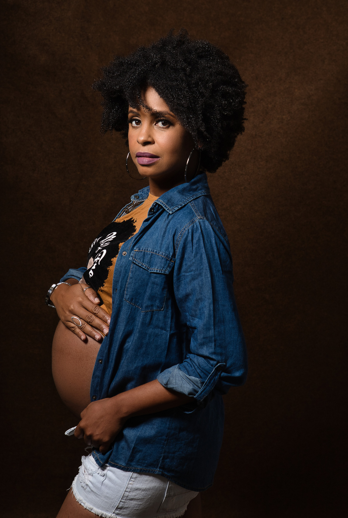 gestante com camisa e jaqueta jeans abraçando a barriga 