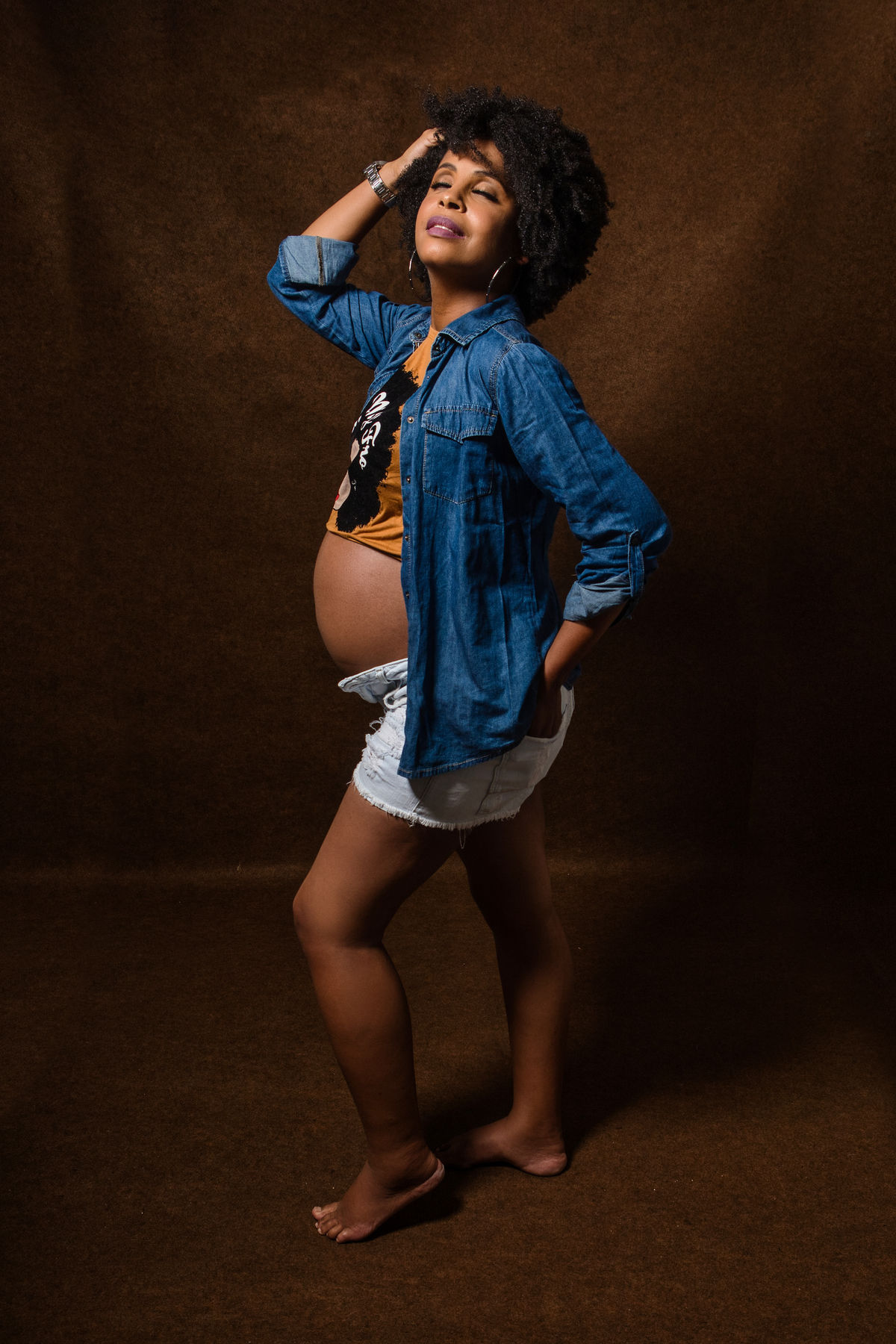 gestante com camisa, bermuda e jaqueta jeans com mão no bolso e outra na cabeça