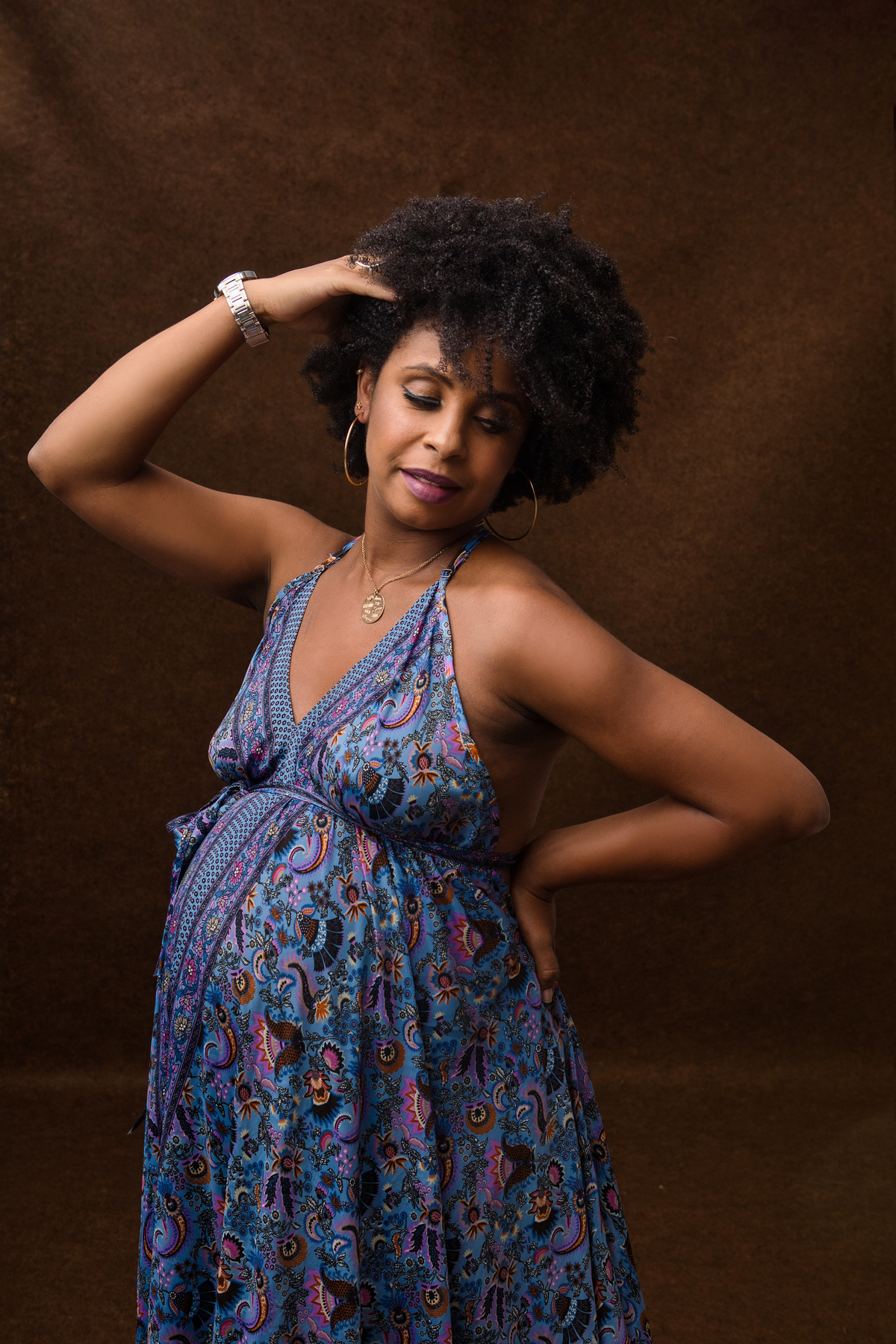 gestante de vestido longo com mão na cintura e outra no cabelo