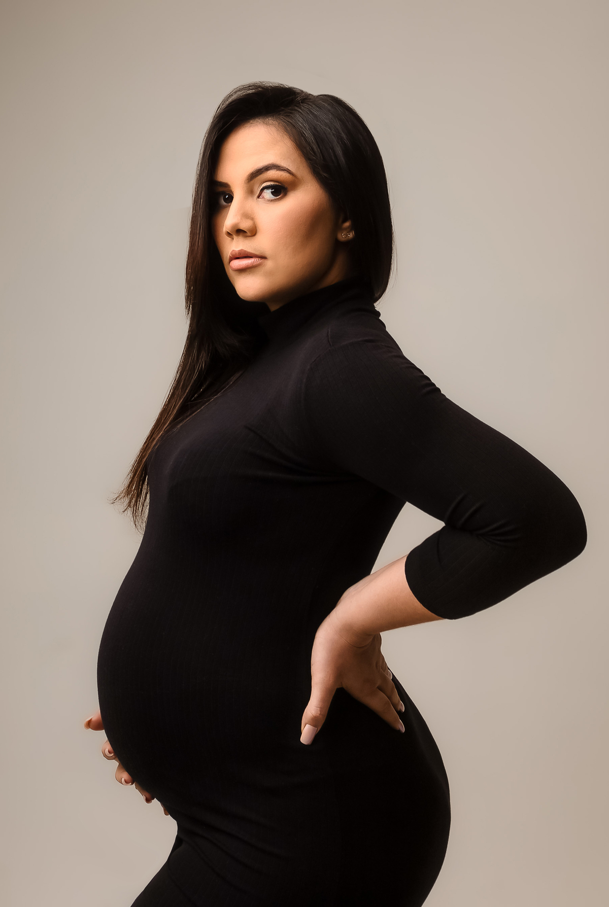 gestante com vestido preto de perfil com  mão na barriga e outra na cintura