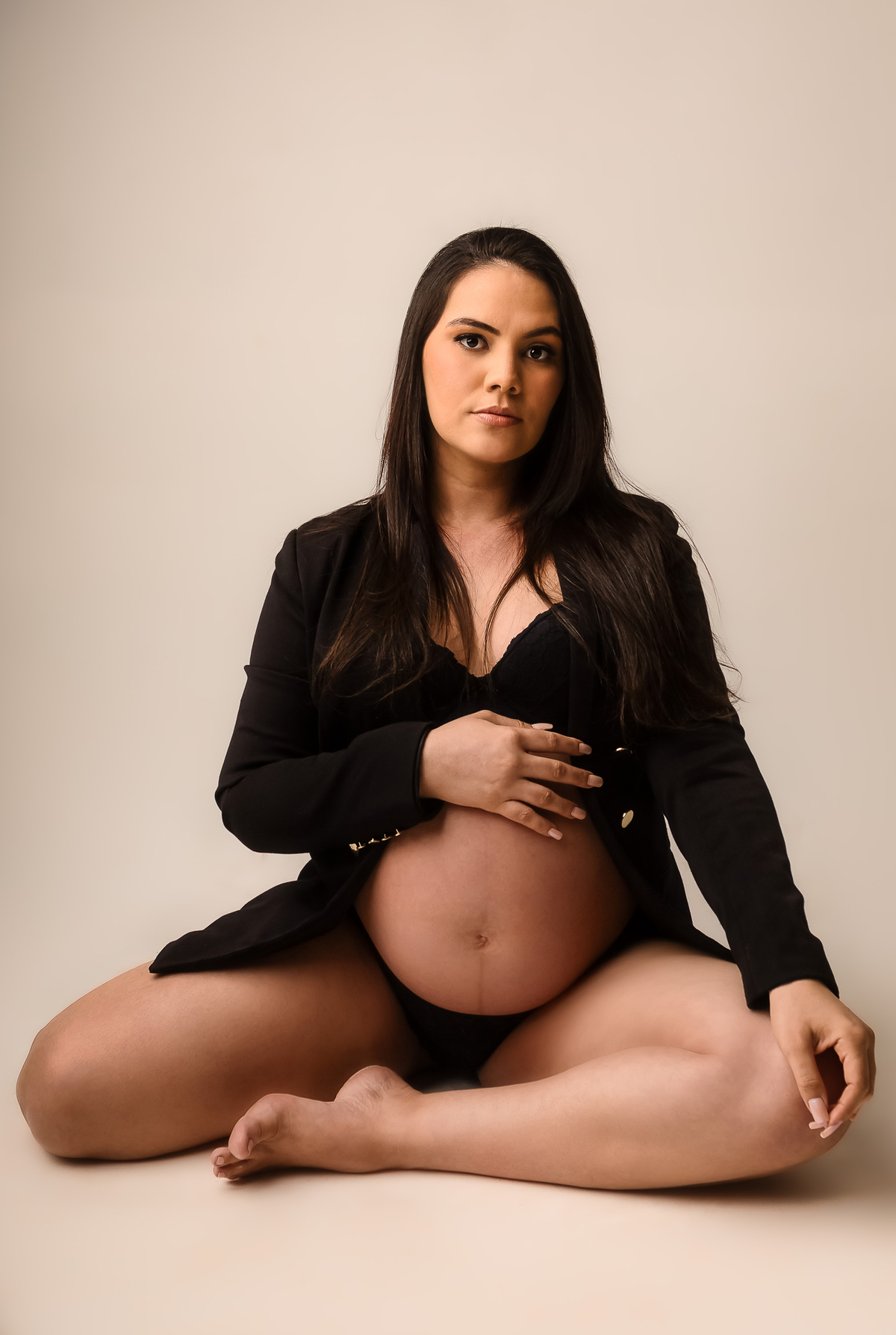 gestante boudoir sentada com blazer preto tocando a barriga