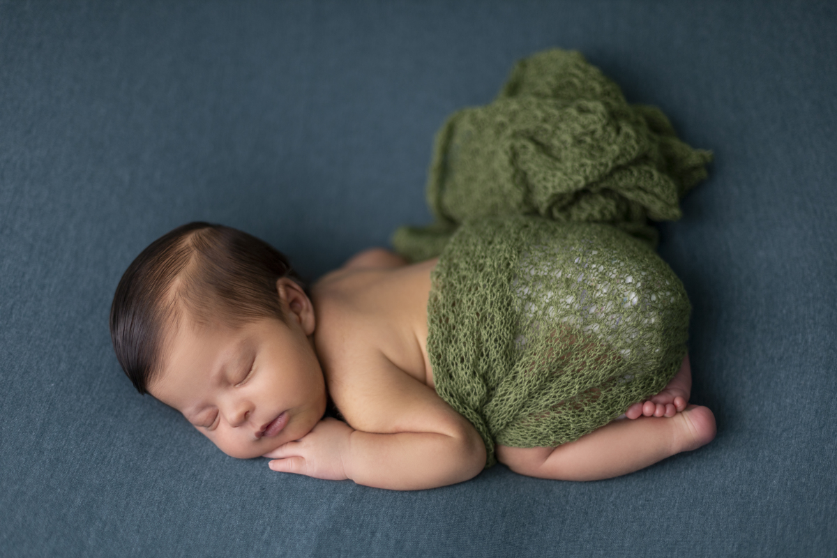 newborn de bruços coberto de lençol verde