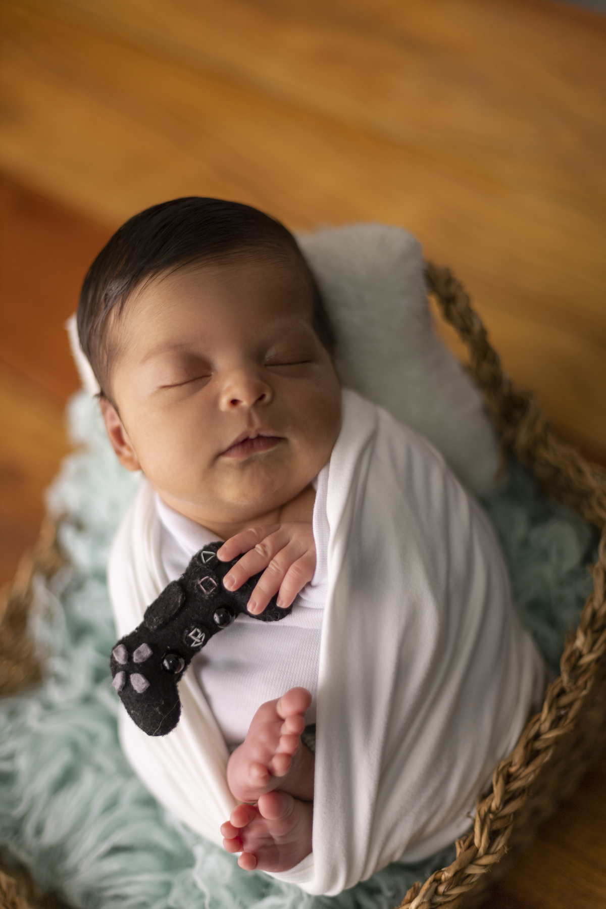 newborn coberto na cesta e segurando controle de video game
