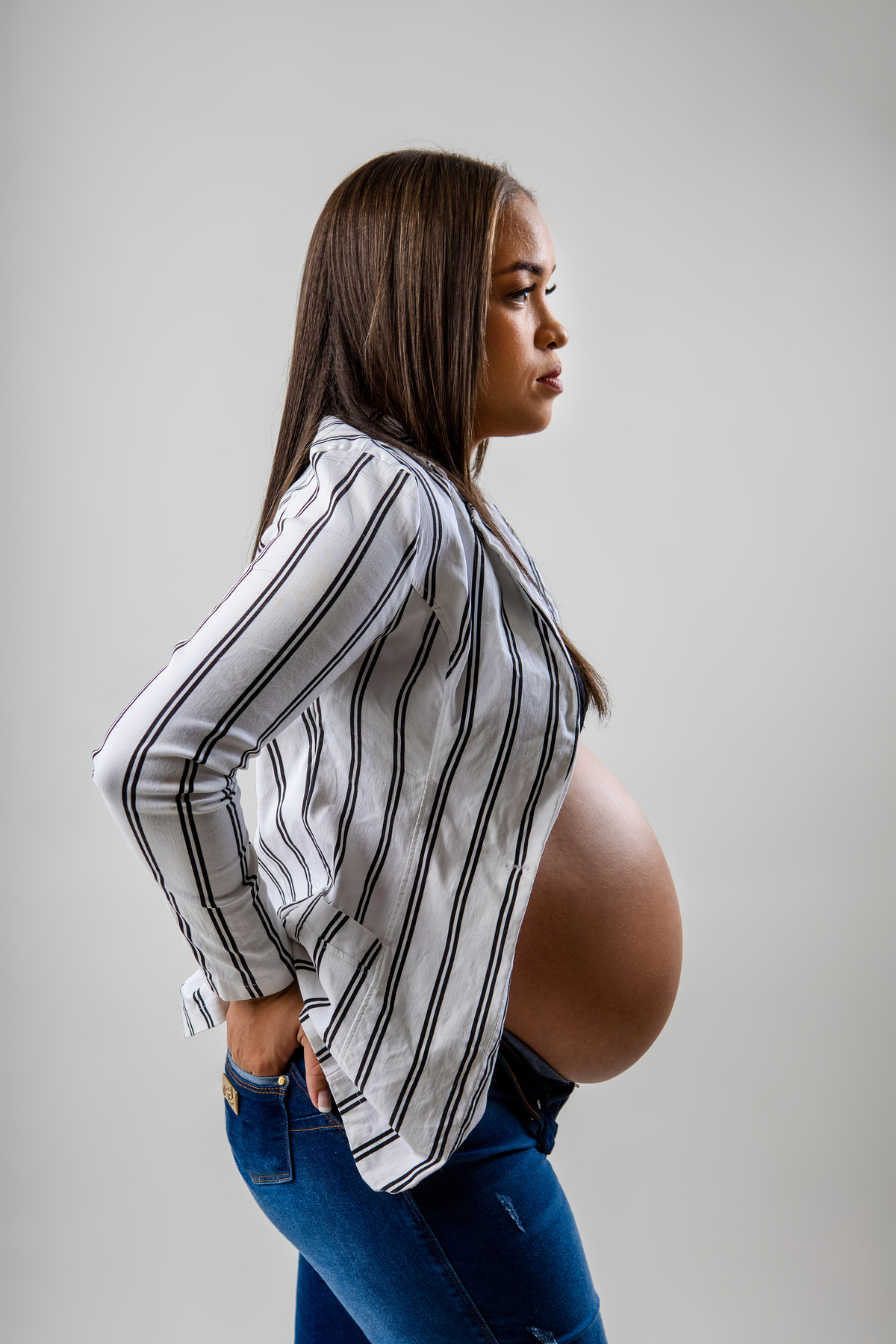 gestante de calça jeans e blazer de perfil com mão do bolso