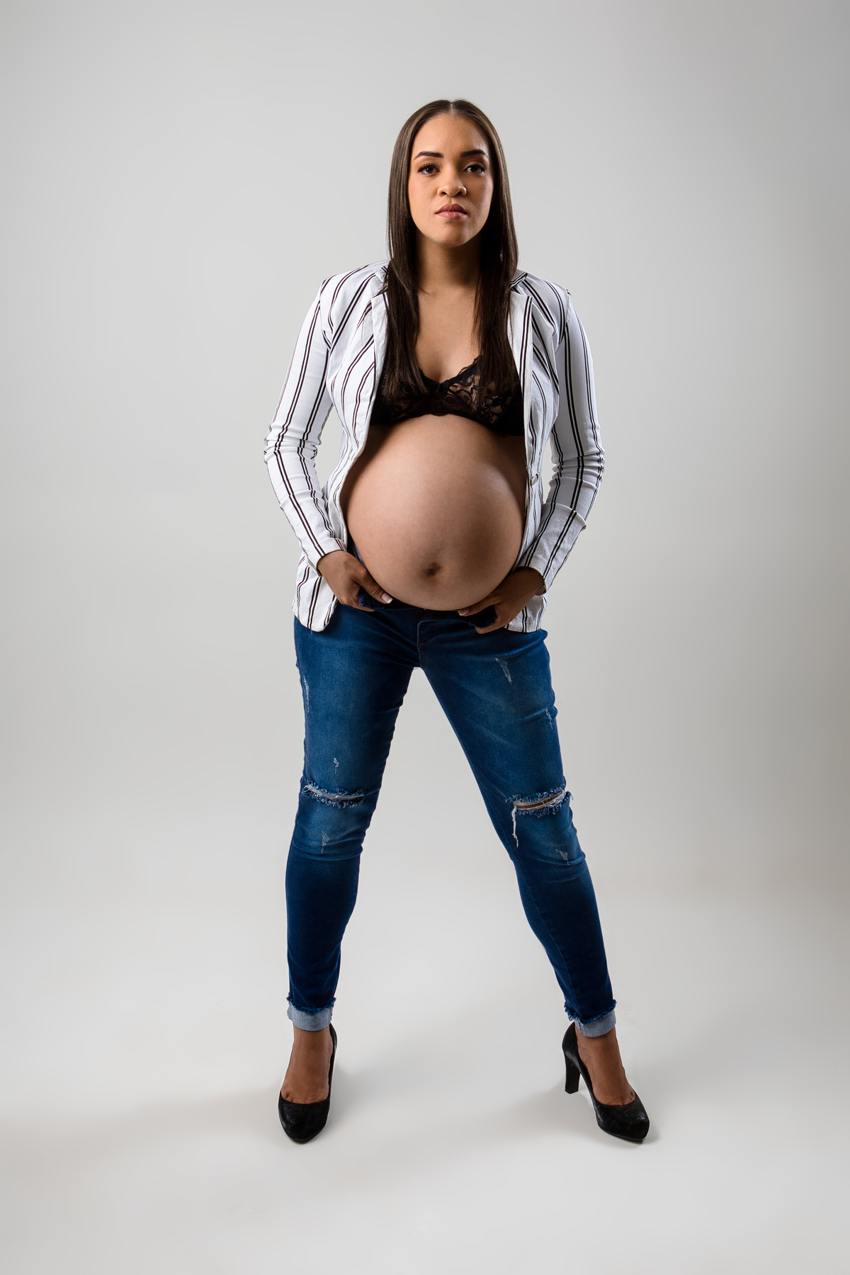 gestante de calça jeans e blazer segurando a abertura da calça