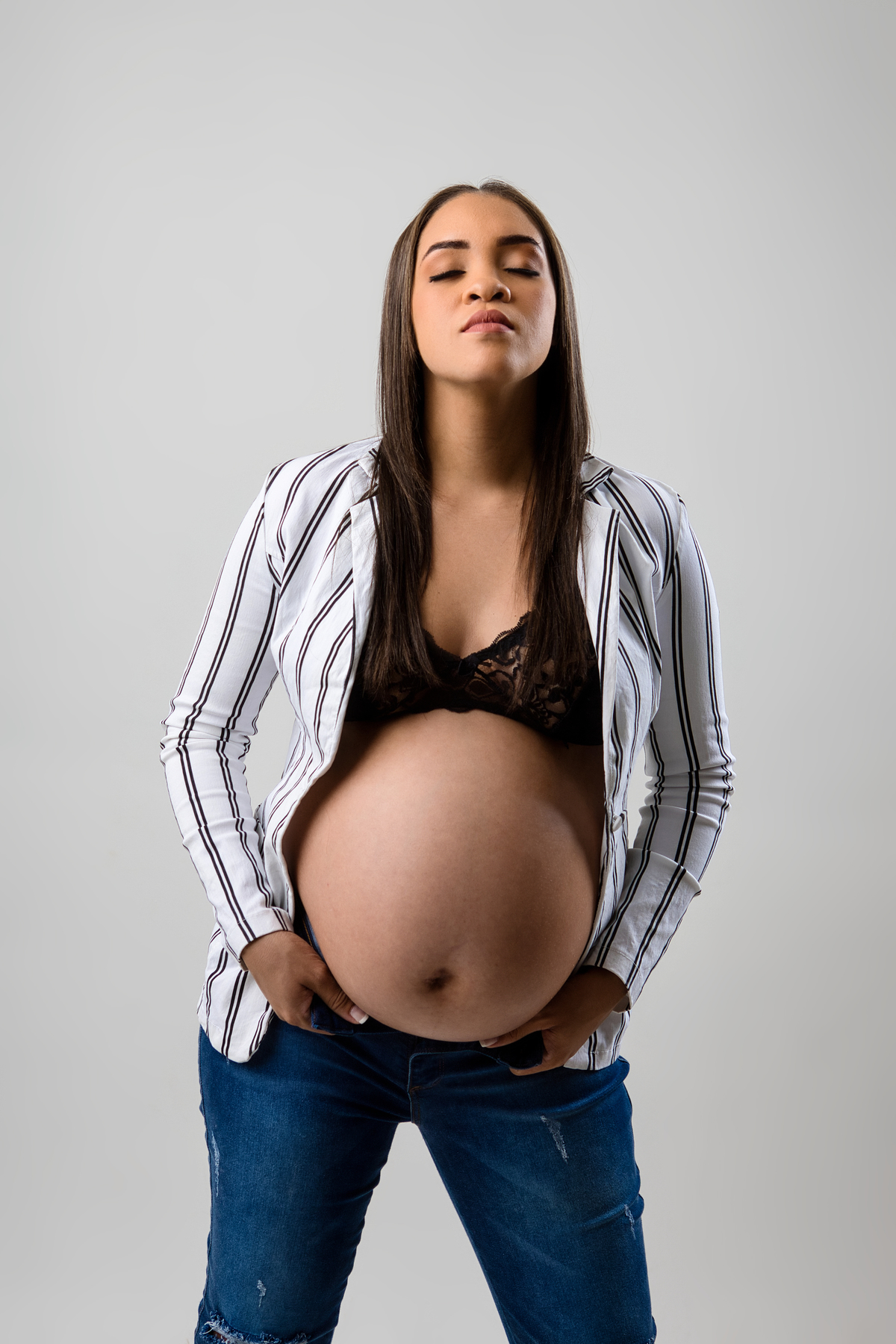 gestante de calça jeans e blazer segurando a abertura da calça