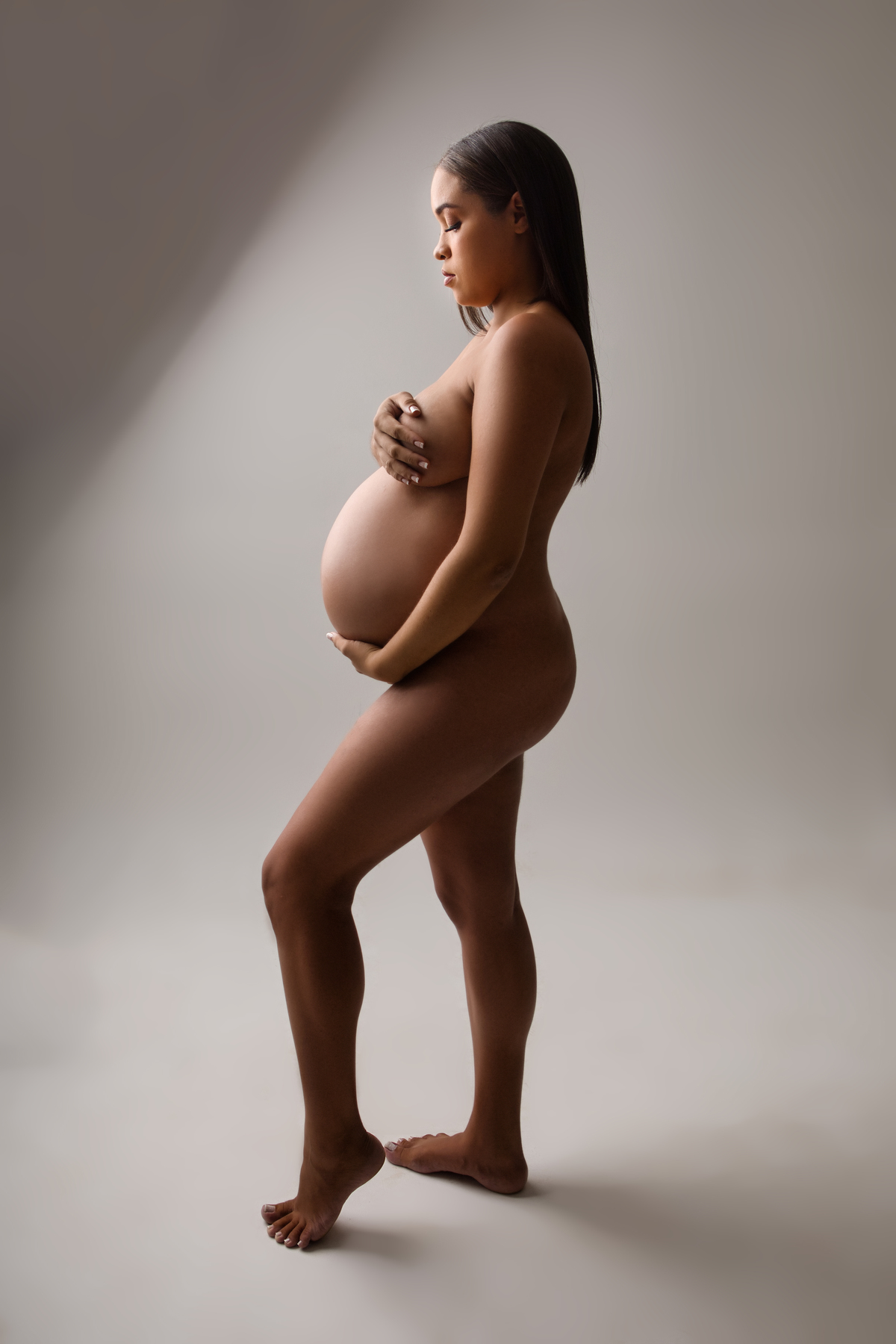 gestante boudoir de perfil com as mãos do peito e barriga