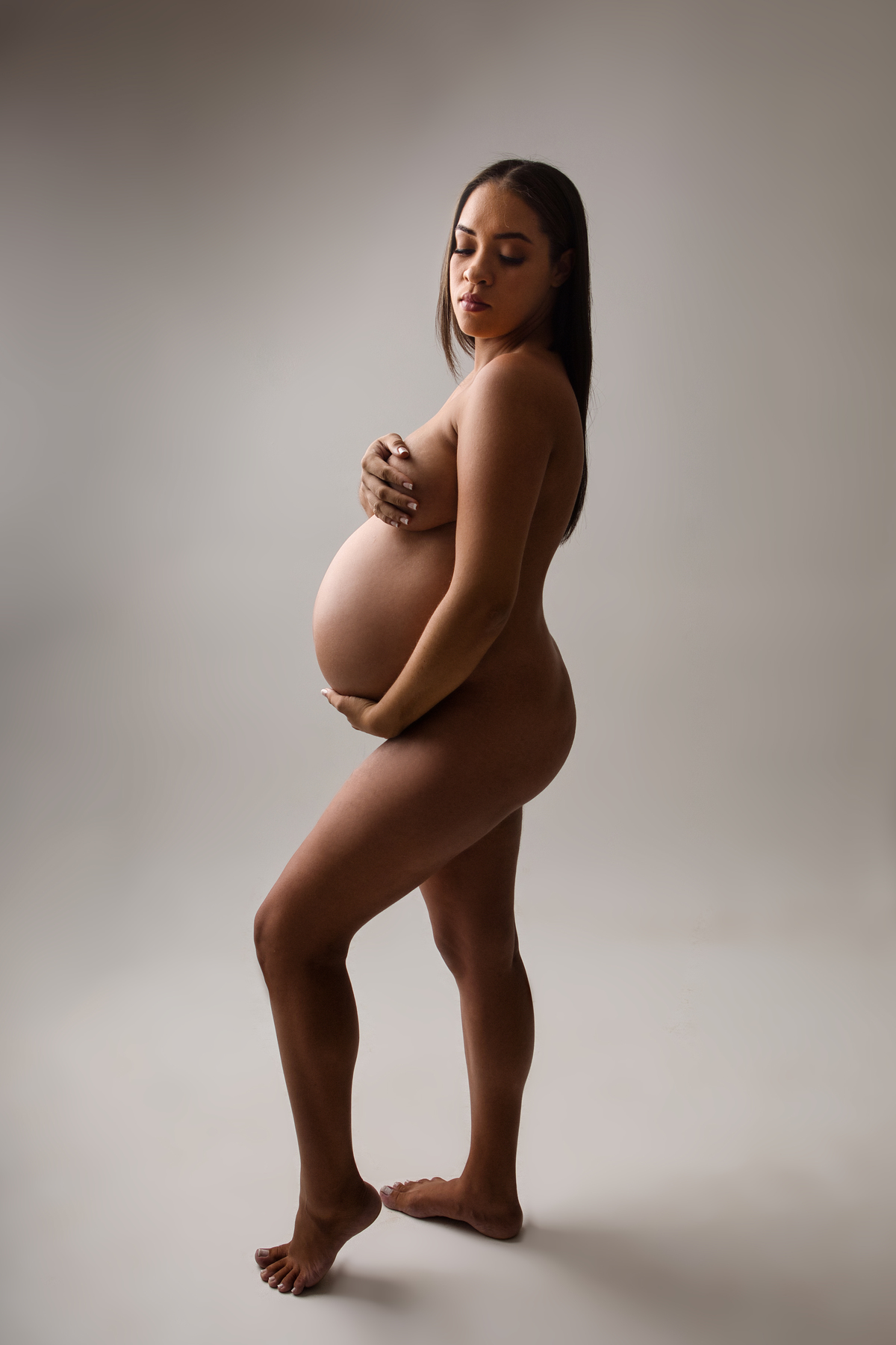 gestante boudoir de perfil com as mãos do peito e barriga