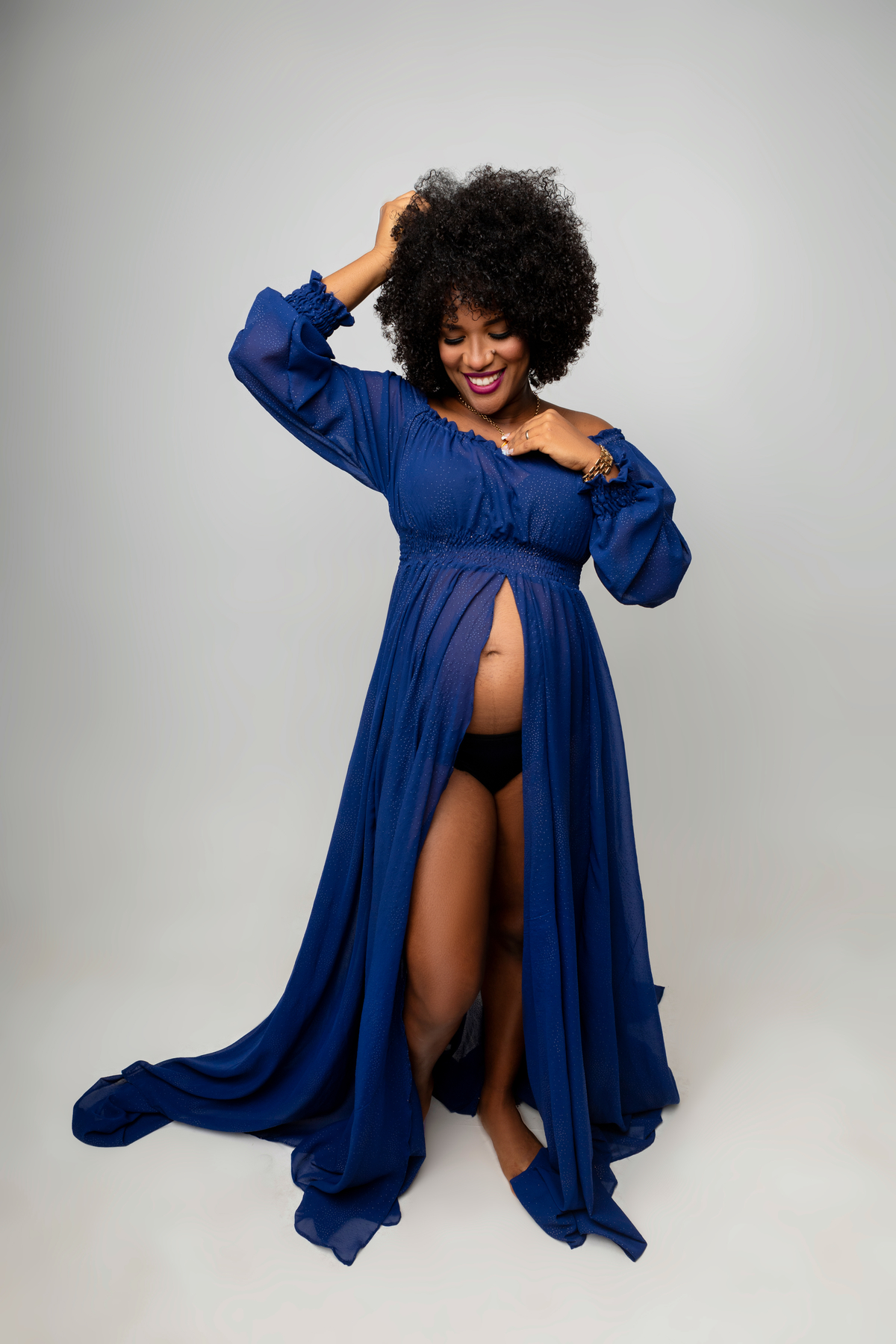 gestante de vestido segurando o cabelo e o colar, e olhando para barriga