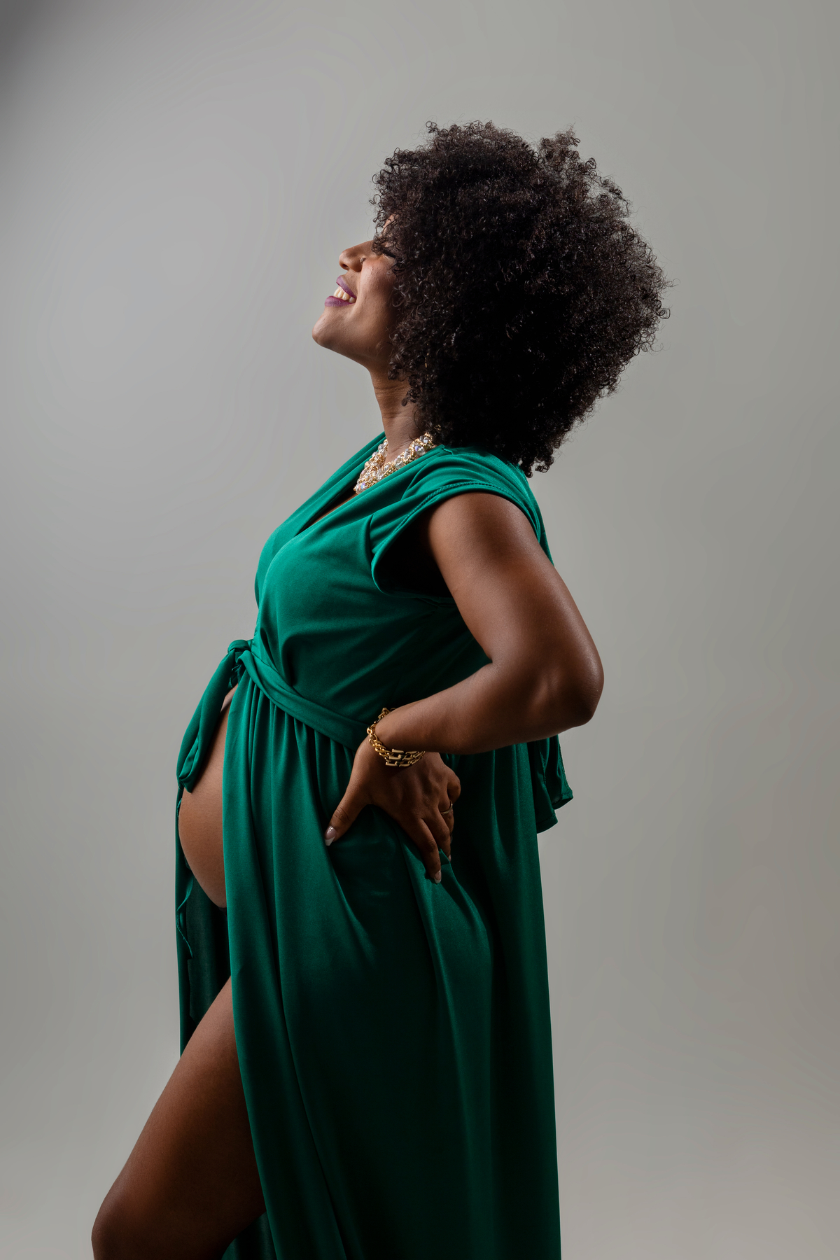 gestante de vestido de perfil com as mãos na cintura