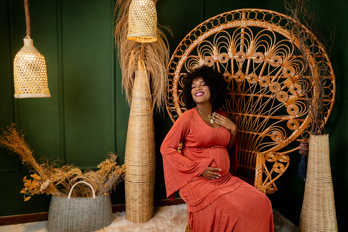 gestante de vestido sentada com a mão na barriga e outra no colar