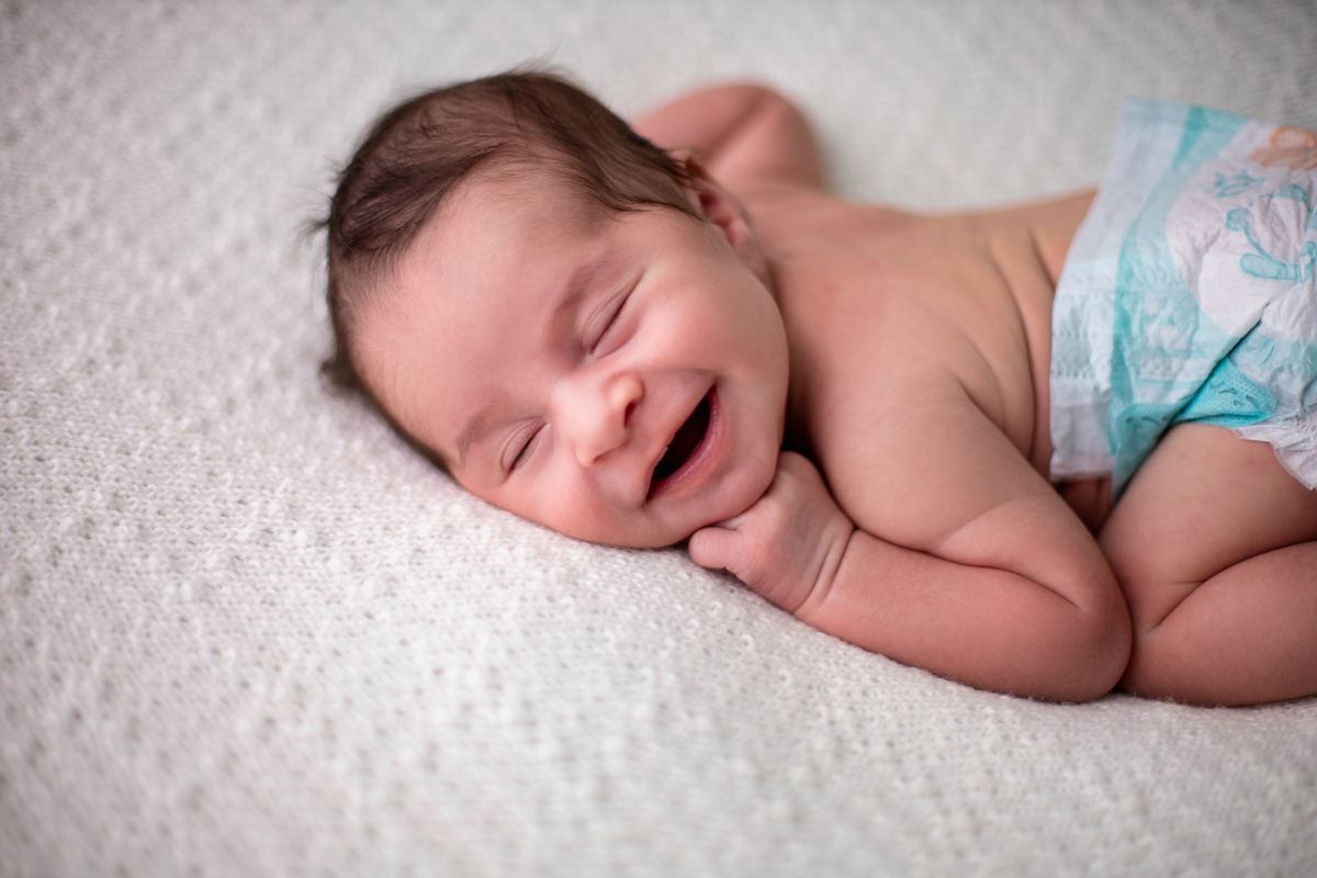 newborn sorridente de bruços e fralda
