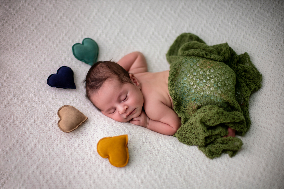 newborn de bruços com lençol e corações