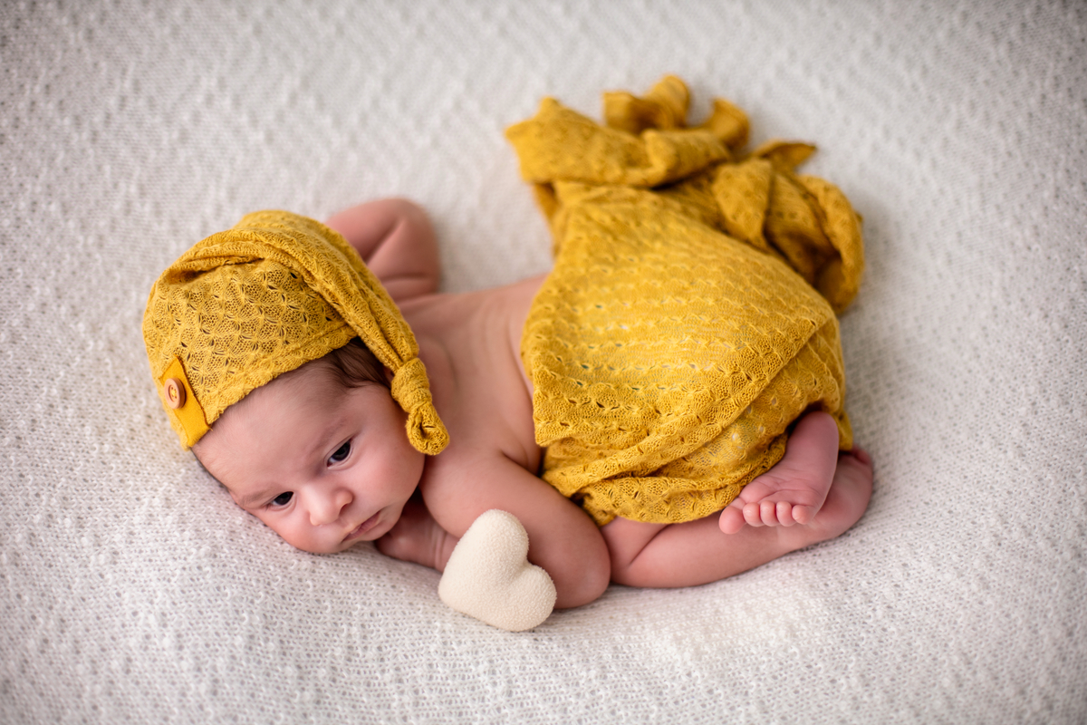 newborn de bruços com lençol e gorro amarelo