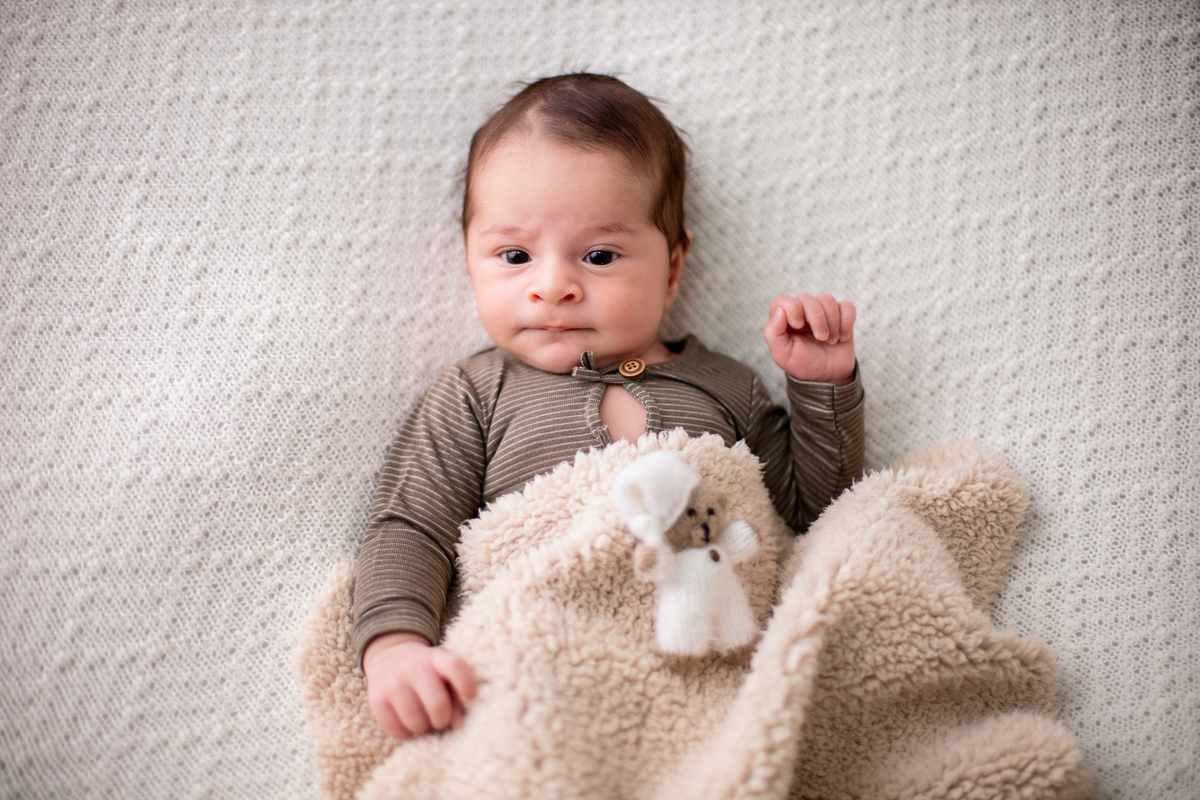 newborn deitado de macaquinho com cobertor e ursinho de pelúcia