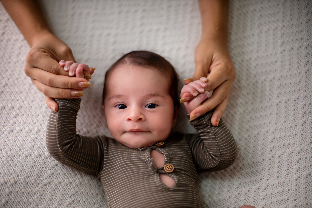 newborn deitado segurando as mãos da mamãe