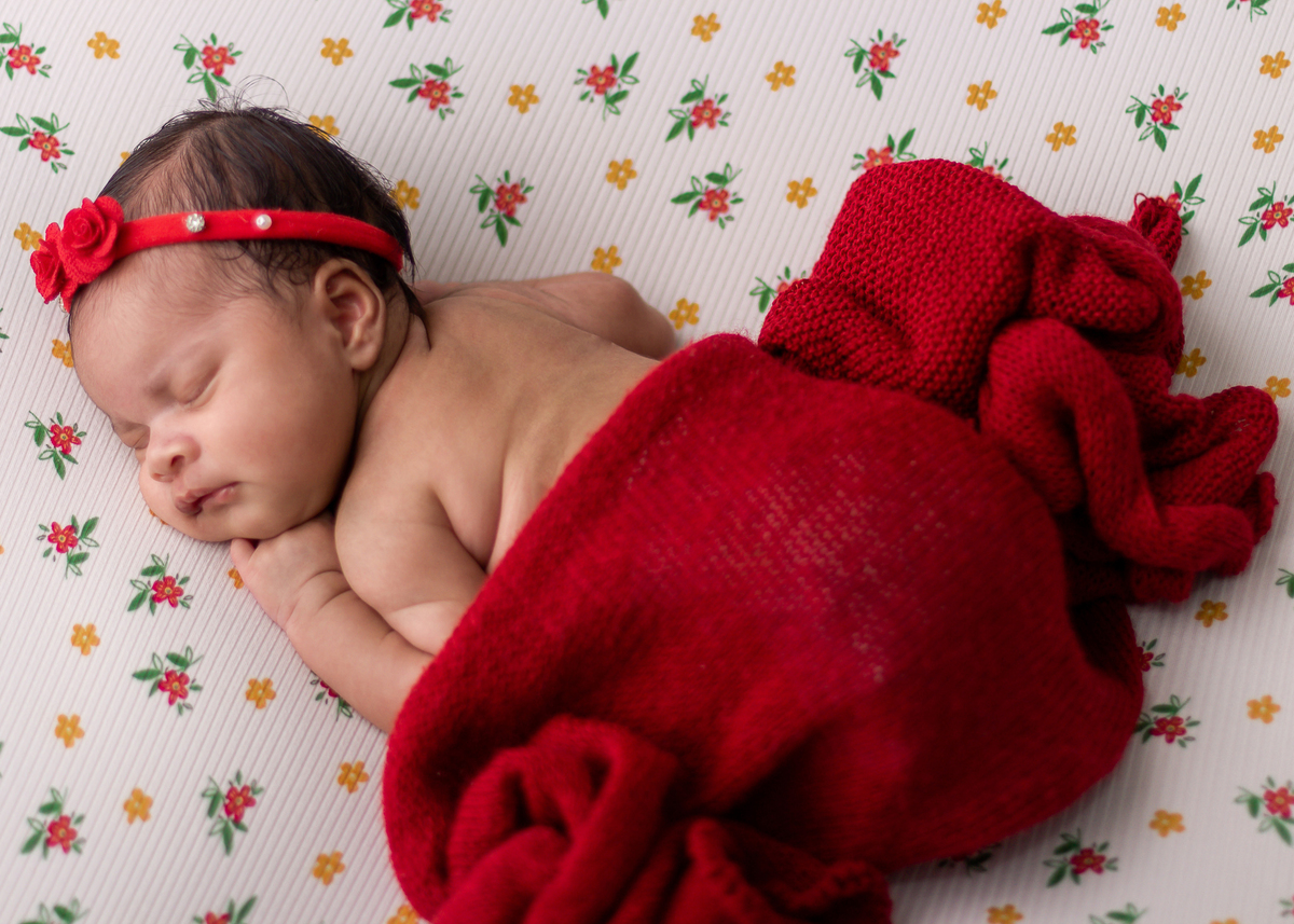 newborn de bruços coberto com lençol e tiara