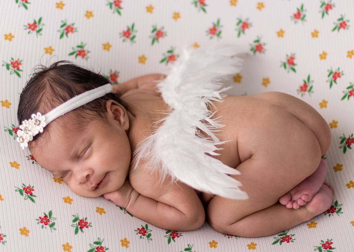newborn de bruços com tiara e asas de anjo