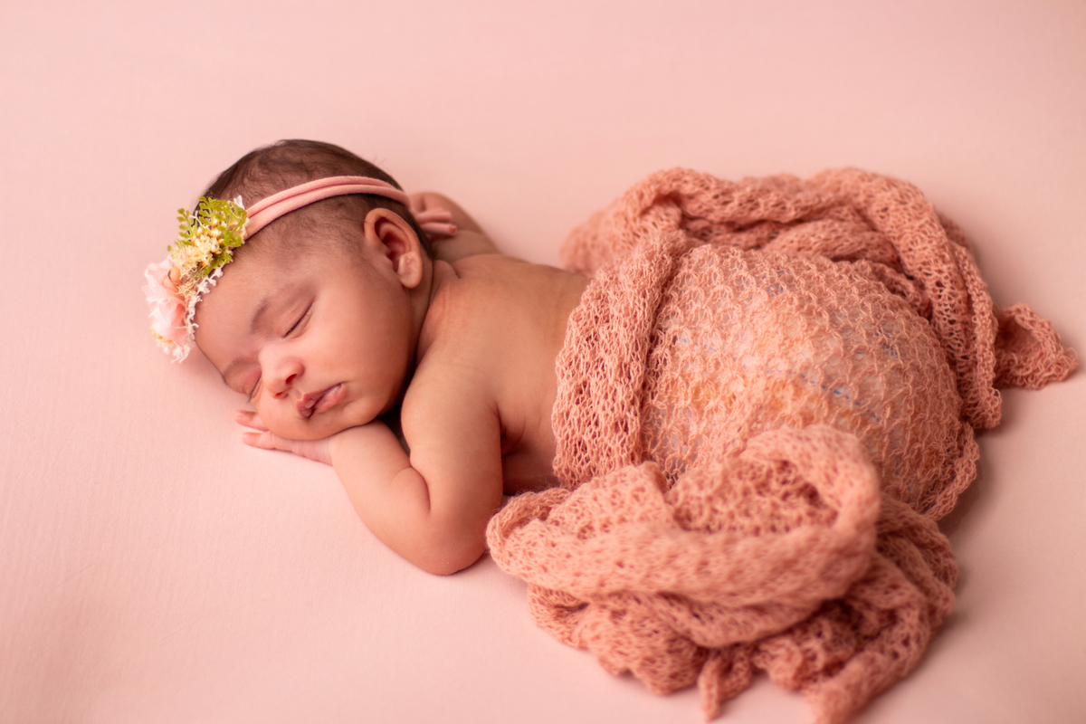 newborn de bruços com lençol bege e tiara