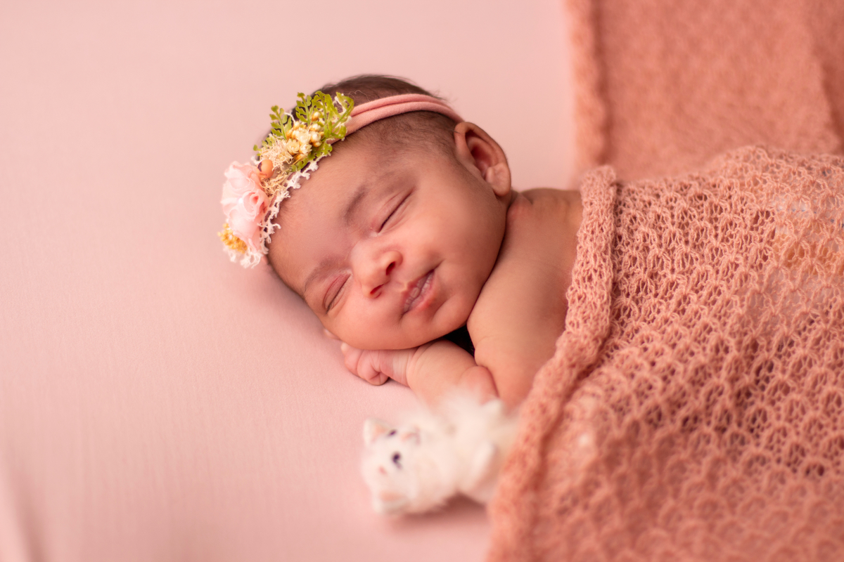 newborn de bruços com lençol bege, tiara e gatinho de pelúcia