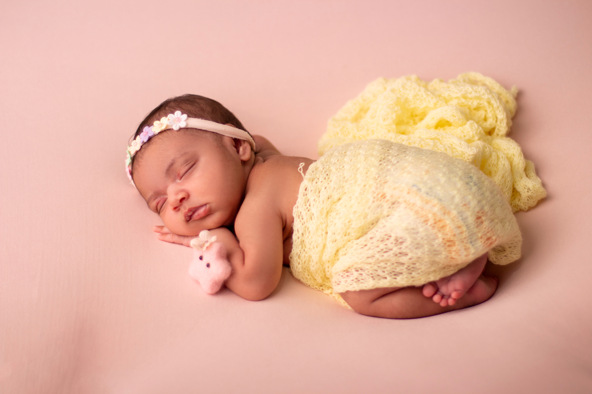 newborn de bruços com lençol amarelo, tiara e estrela de pelúcia