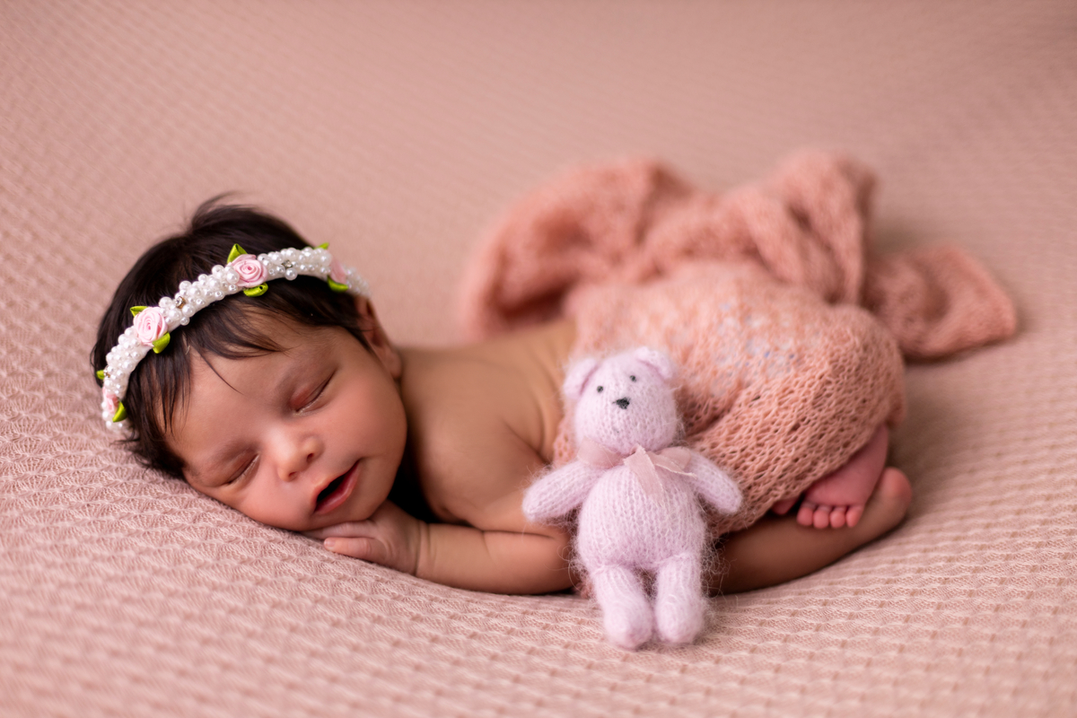 newborn de bruços com tiara, lençol e ursinho de pelúcia