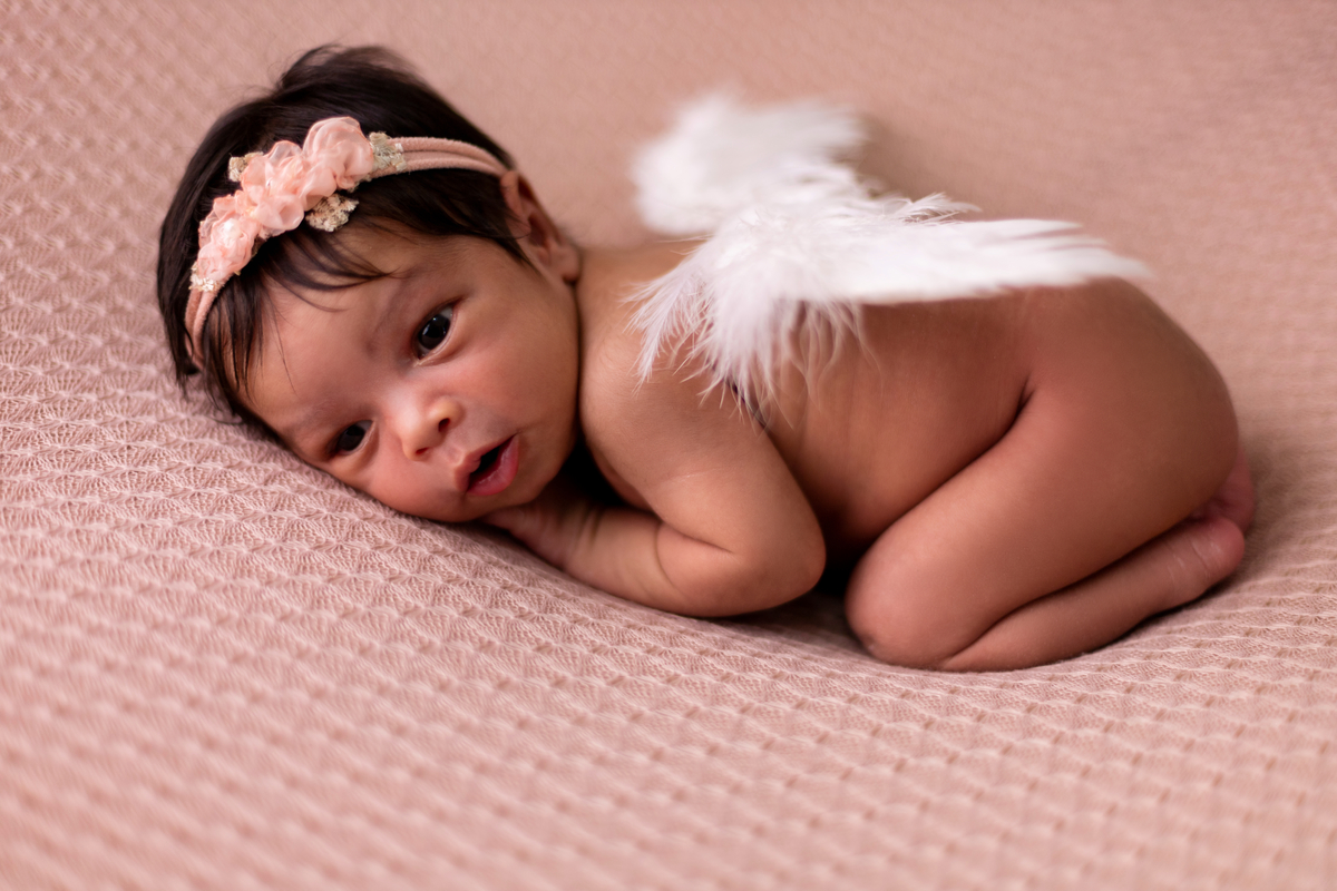 newborn de bruços com tiara e asas de anjo