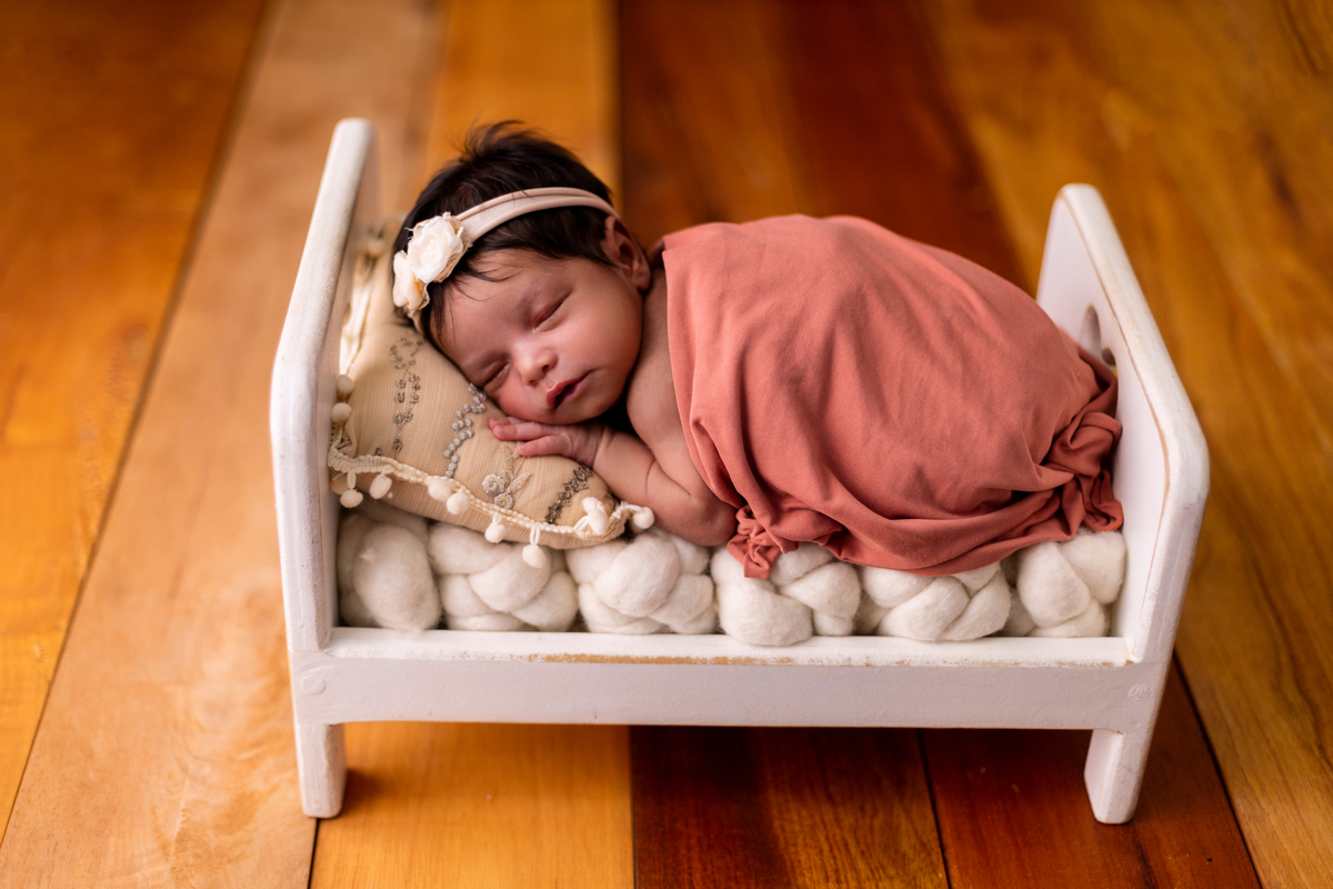 newborn de bruços com props cama e coberto com lençol