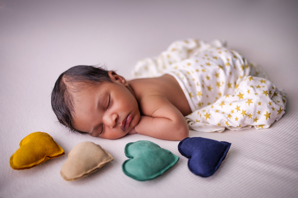 newborn de bruços com lençol e corações 