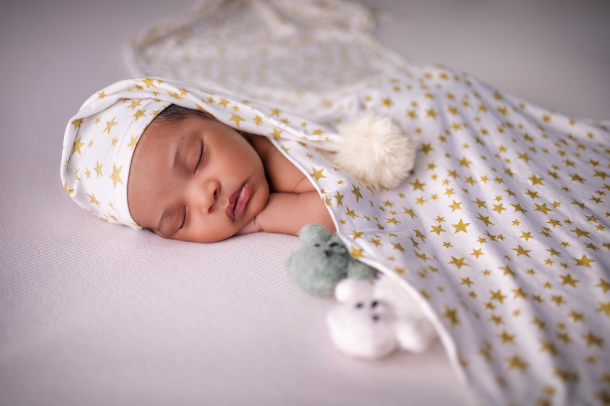 newborn de bruços com lençol, gorro e seus bichinhos de pelúcia
